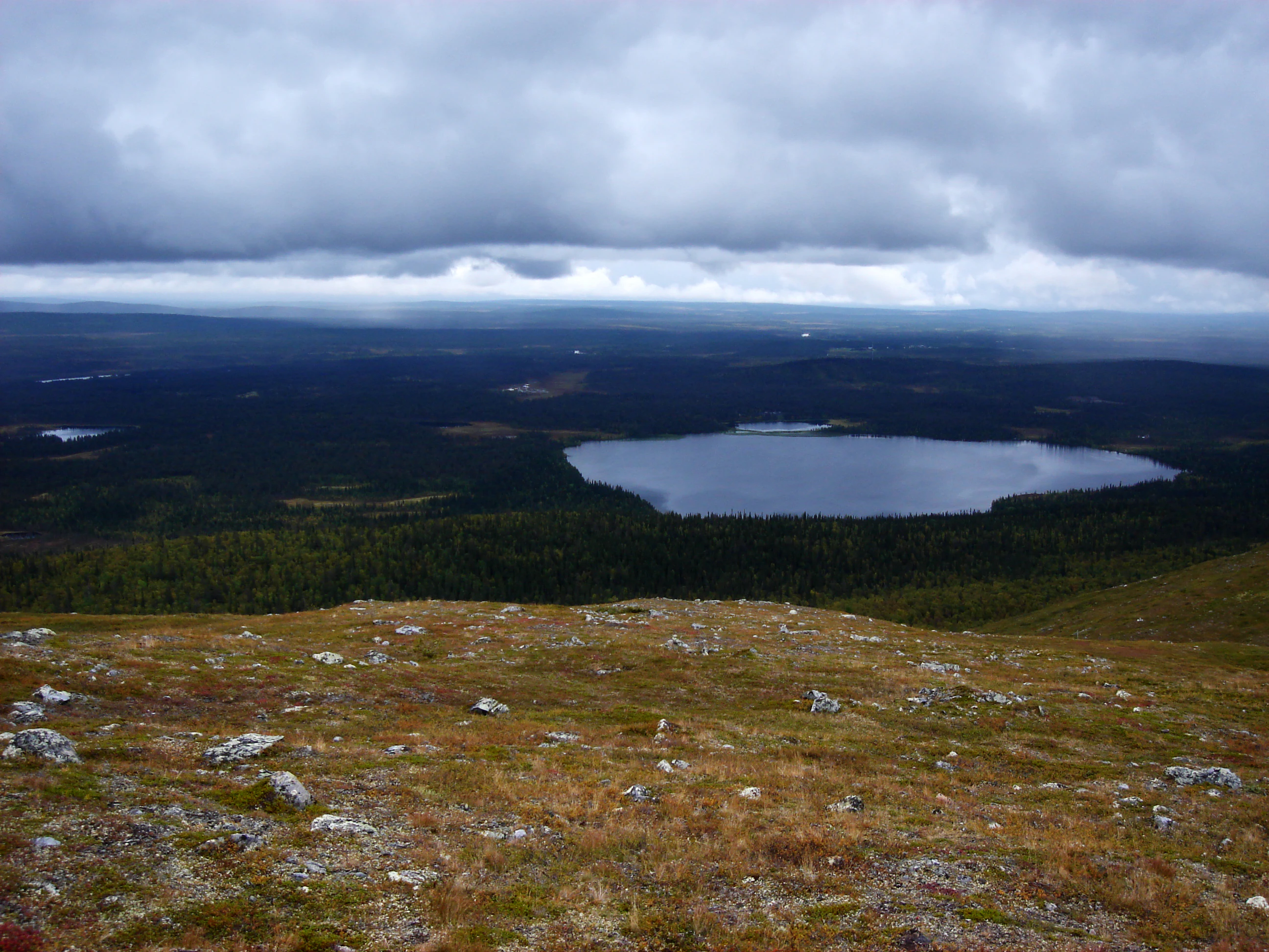 Panoramic view of Lake Vuontisjärvi from a rocky hilltop, surrounded by forested terrain under a cloudy sky