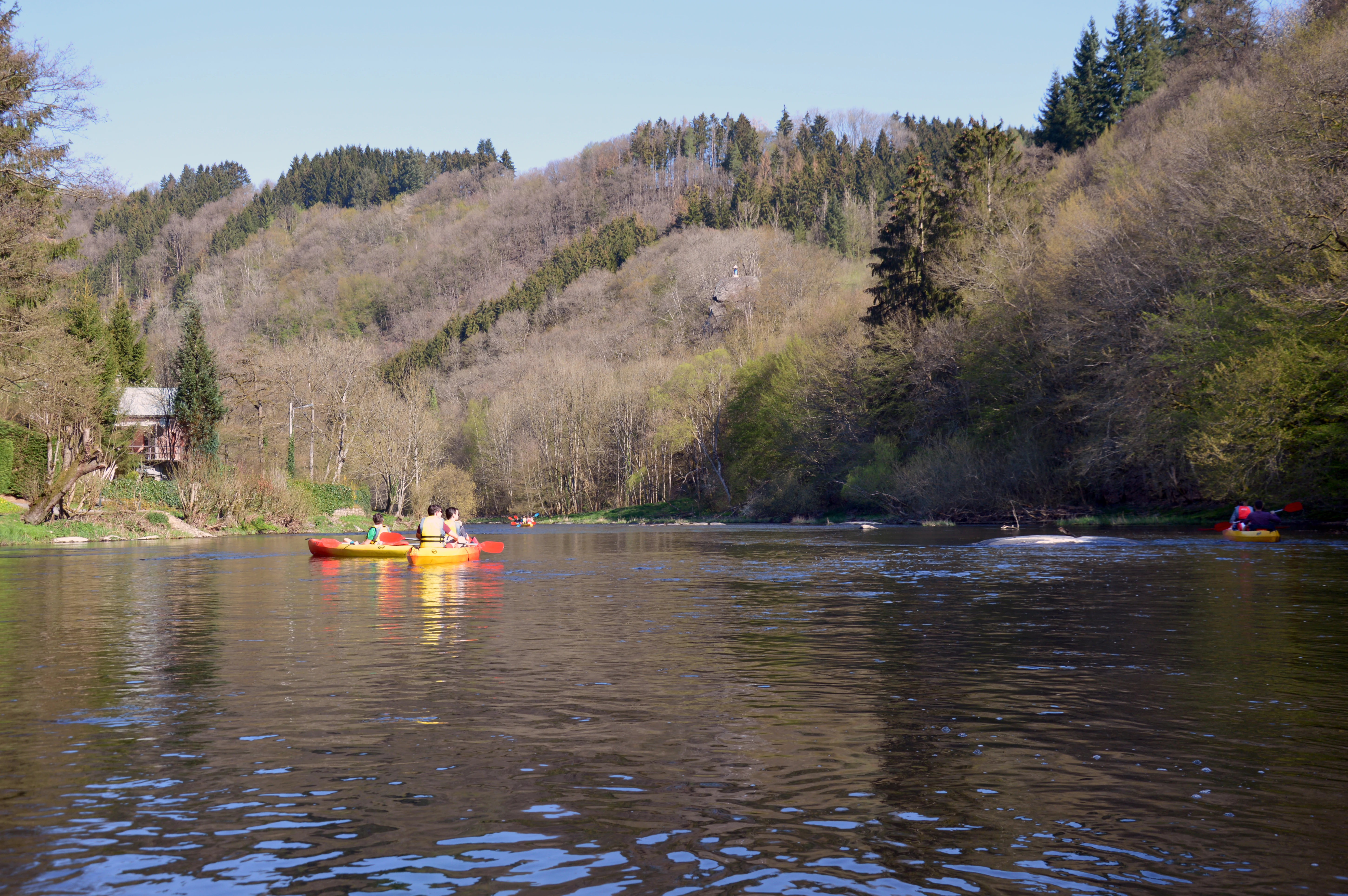 A wide shot of the Ourthe river winding through a valley in the Belgian Ardennes with people kayaking in the foreground.