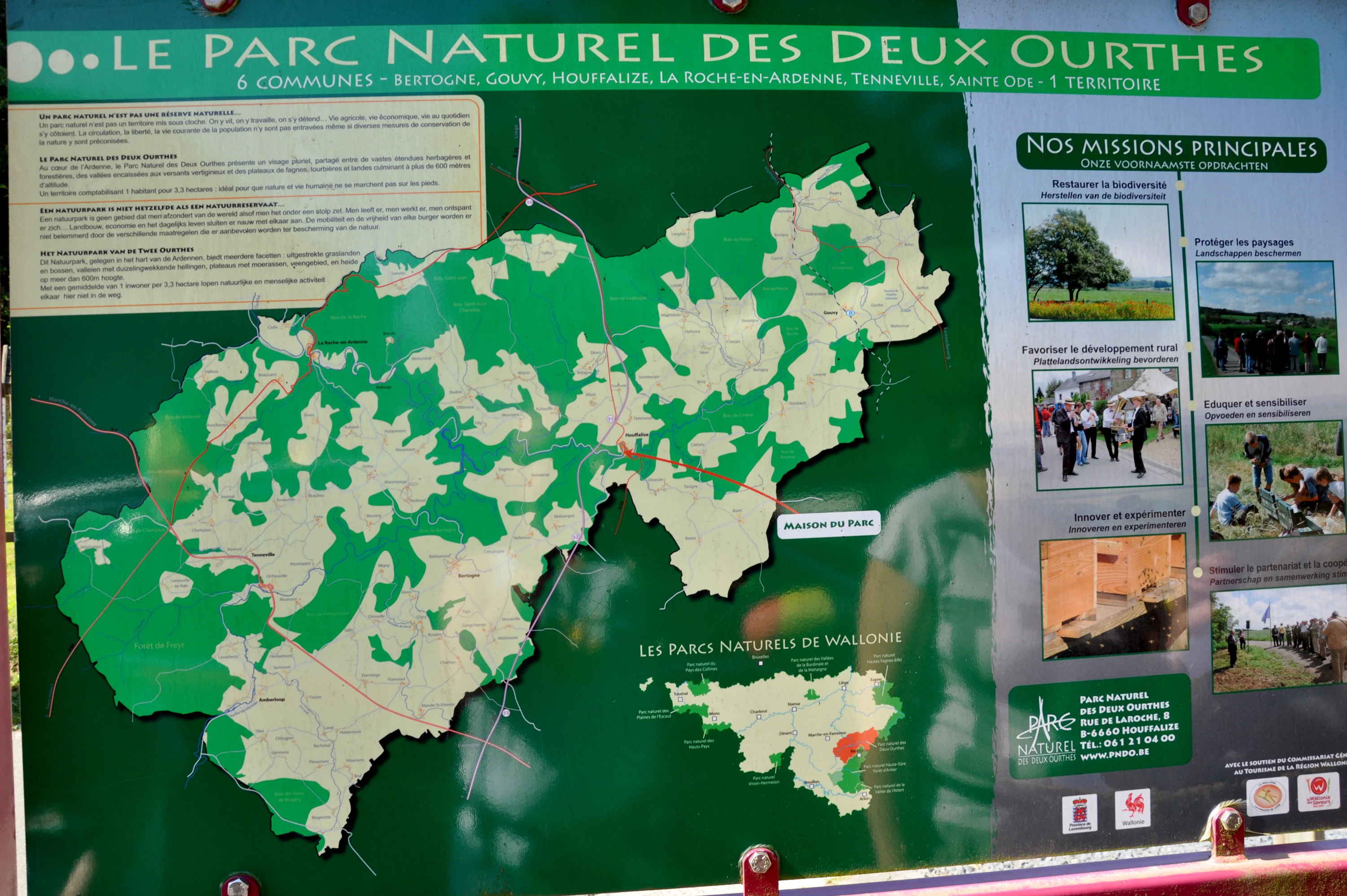 A large park information sign titled Le Parc Naturel des Deux Ourthes featuring a map of the park area, text describing park objectives, and small inset photos of outdoor activities.