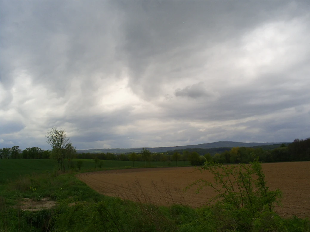 A landscape view of open farmland and distant hills in Poland under a cloudy grey sky.