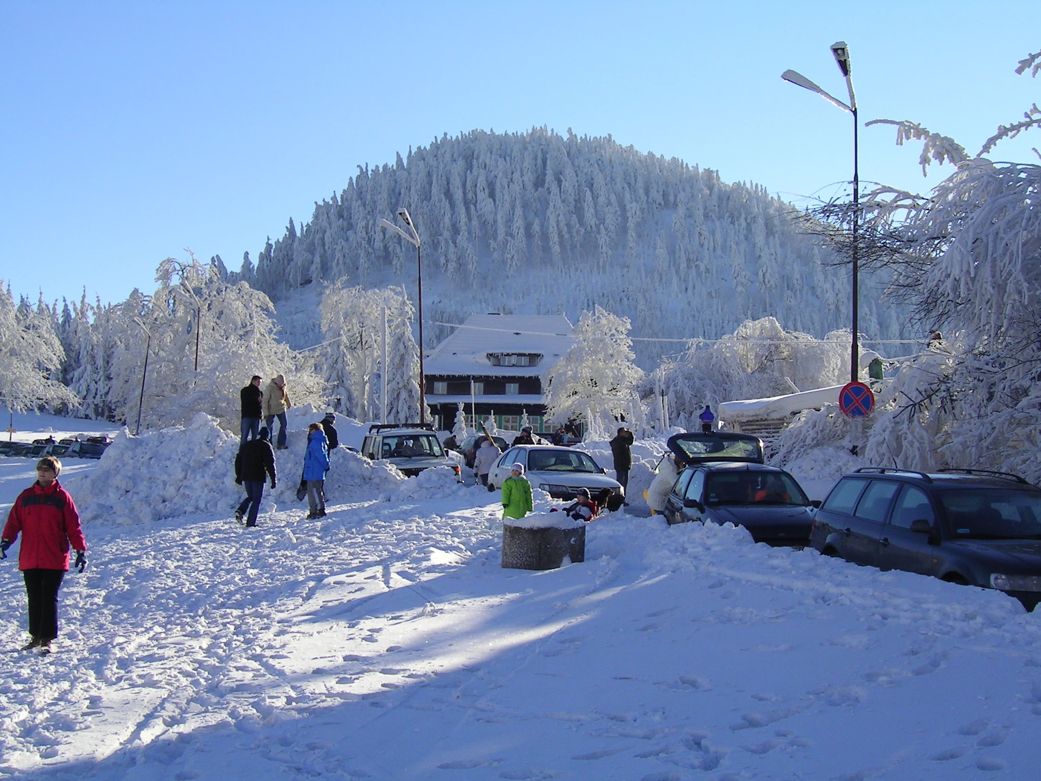 A snow-covered parking area in winter with a forest-covered mountain peak in the background.