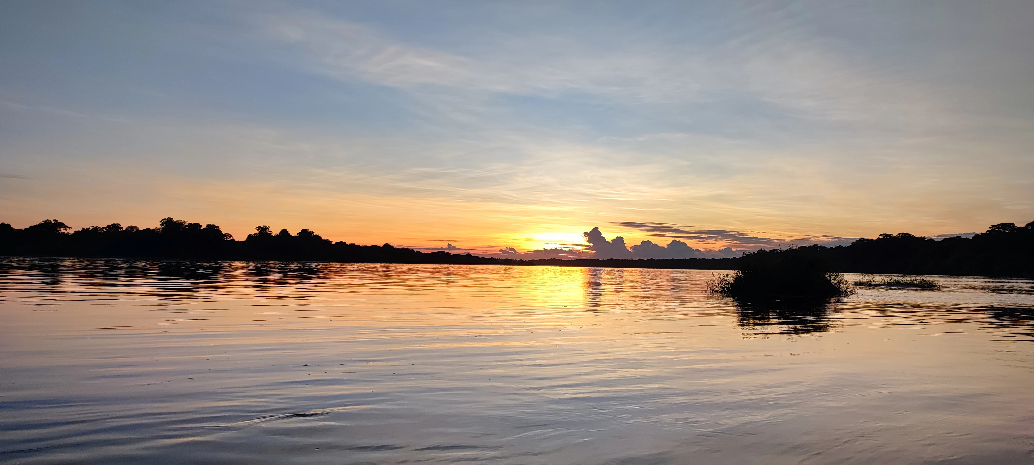 A wide, calm river reflects the orange and blue colors of a sunset, with dark silhouettes of forest lining the distant banks.