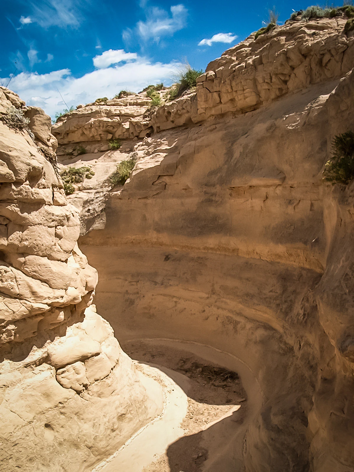 A narrow, winding gully carved into light-colored sedimentary rock under a bright blue sky.