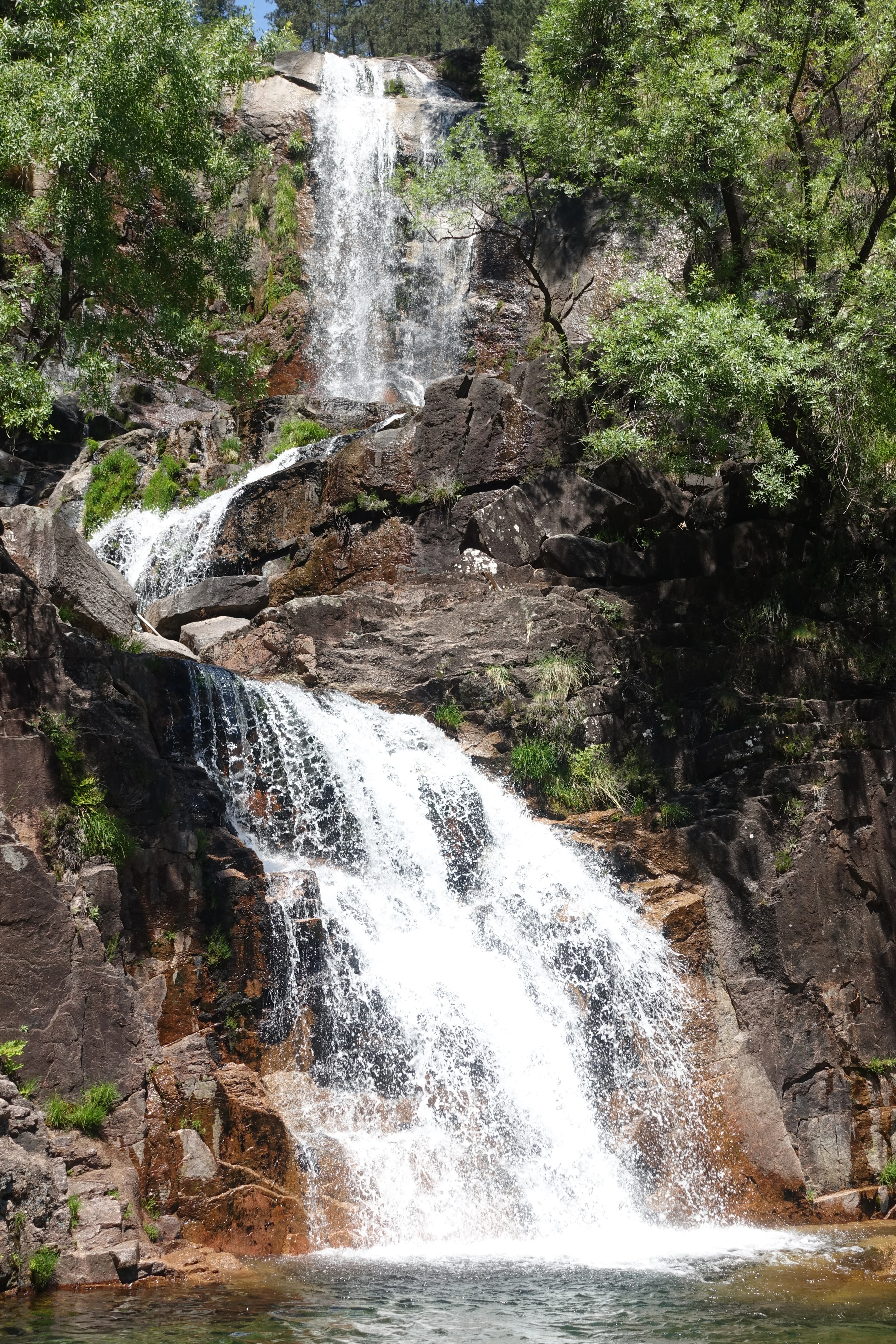 Multi-tiered waterfall flowing down rocky cliffs with green vegetation surrounding the water