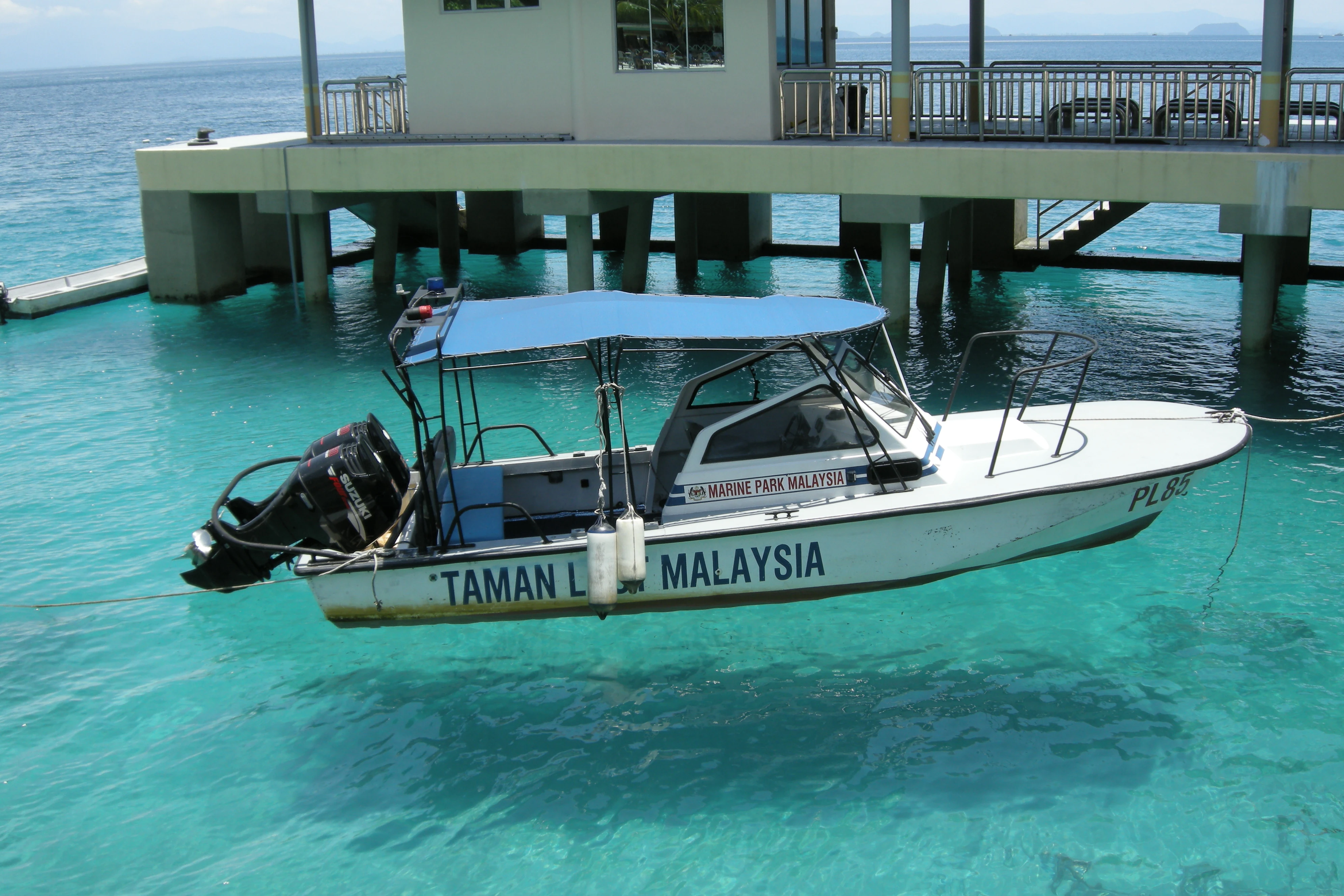 A white motorboat with a blue canopy floating in bright turquoise shallow water next to a pier structure.