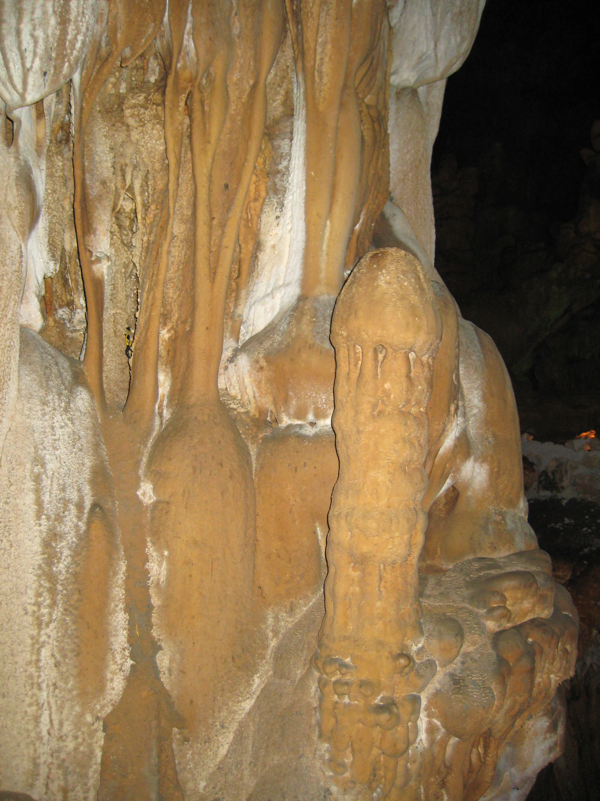 Formaciones de estalagmitas marrones y beige en una cueva, incluyendo una estructura prominente en forma de lingam con depósitos minerales