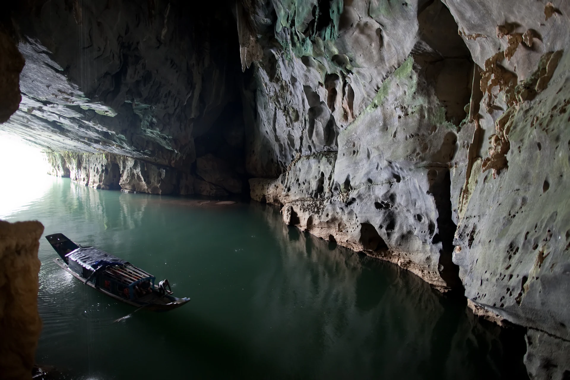Interior de cueva con paredes rocosas, agua tranquila y una barca de madera entrando en una entrada de cueva iluminada