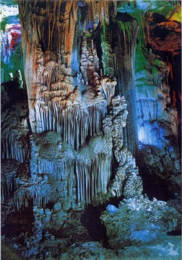 Interior de la cueva Tien Son con estalactitas colgantes y formaciones en las paredes y el suelo de la cueva, iluminada con luz azul y verde