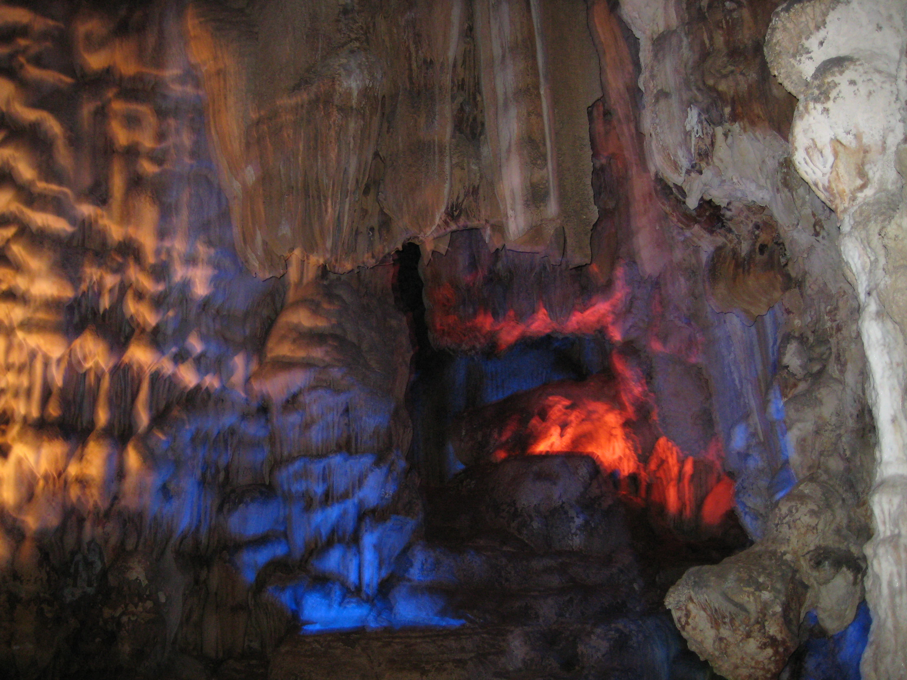 Interior de la cueva que muestra estalactitas y estalagmitas iluminadas con luces azules y rojas
