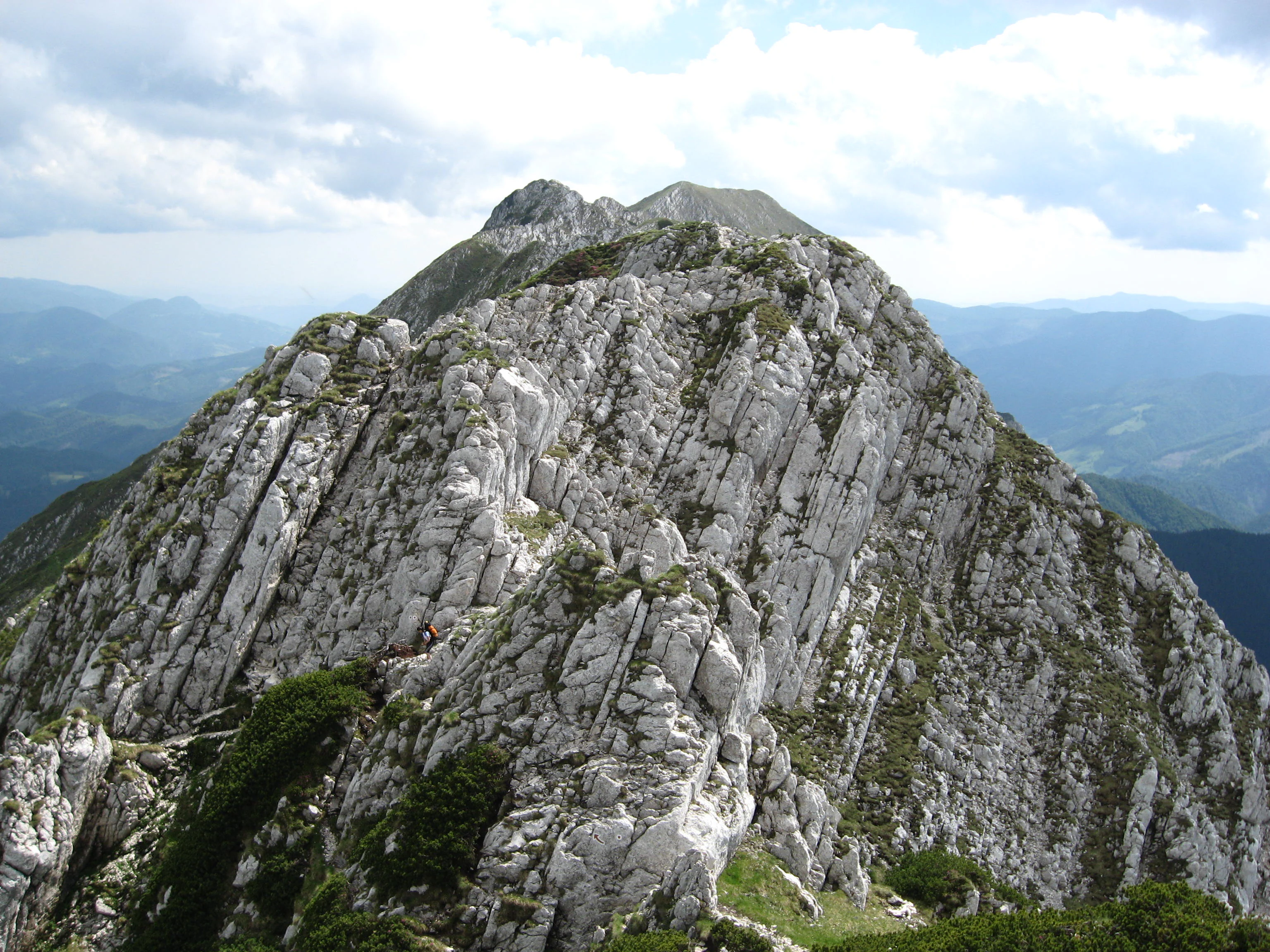 A rocky mountain ridge with steep cliffs and patches of green vegetation under a partly cloudy sky