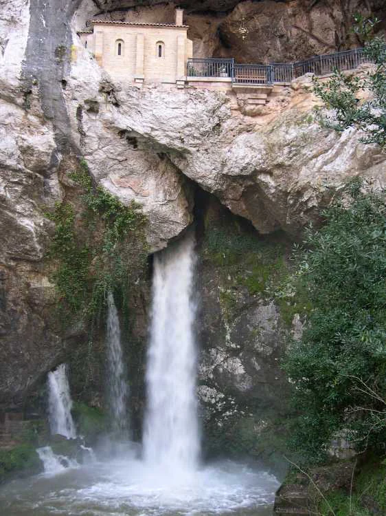Waterfall cascading down rocky cliffs with a small shrine structure built into the rock face