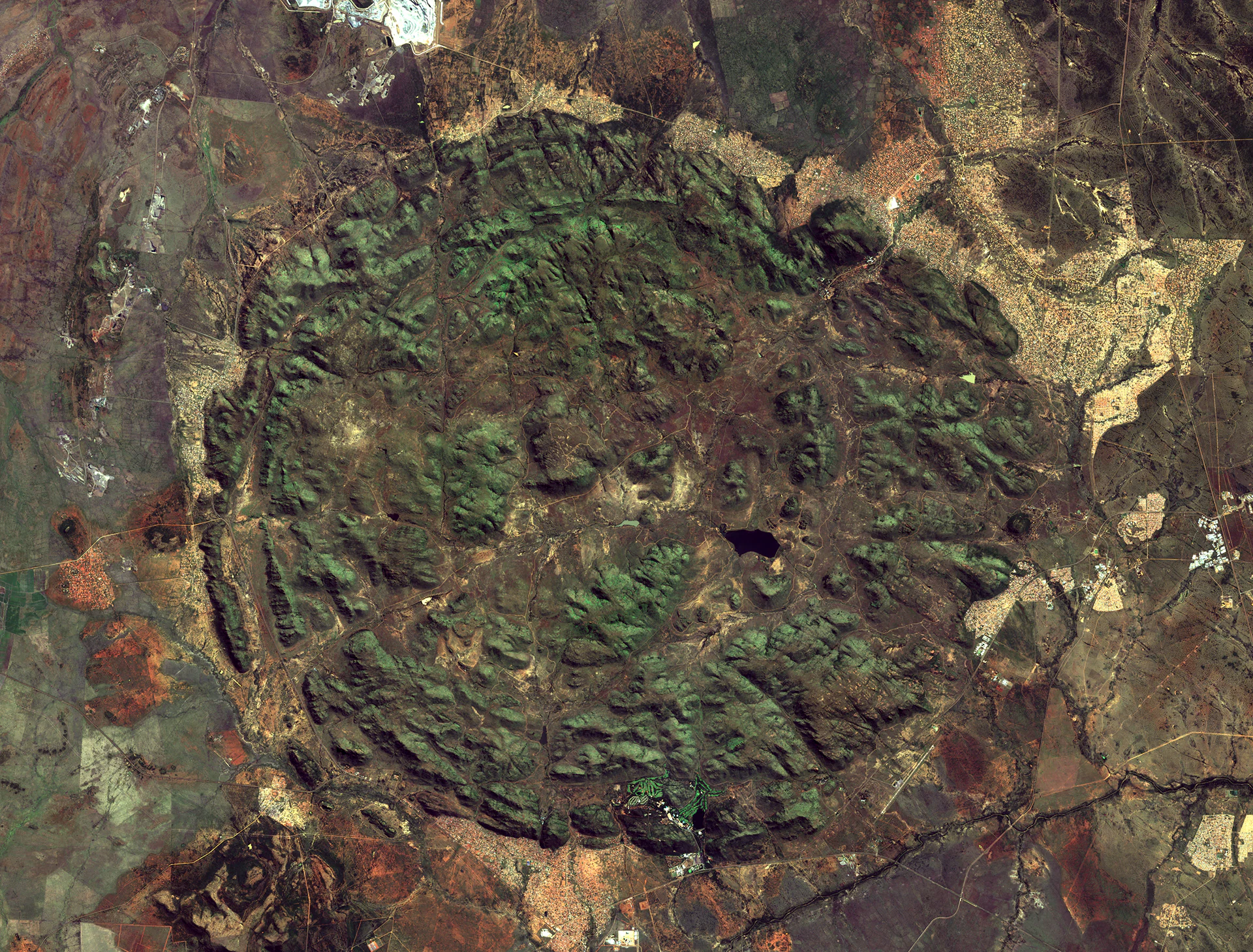 Satellite imagery showing the circular geologic footprint of Pilanesberg National Park in South Africa with its green ridges and valleys set against the surrounding terrain.