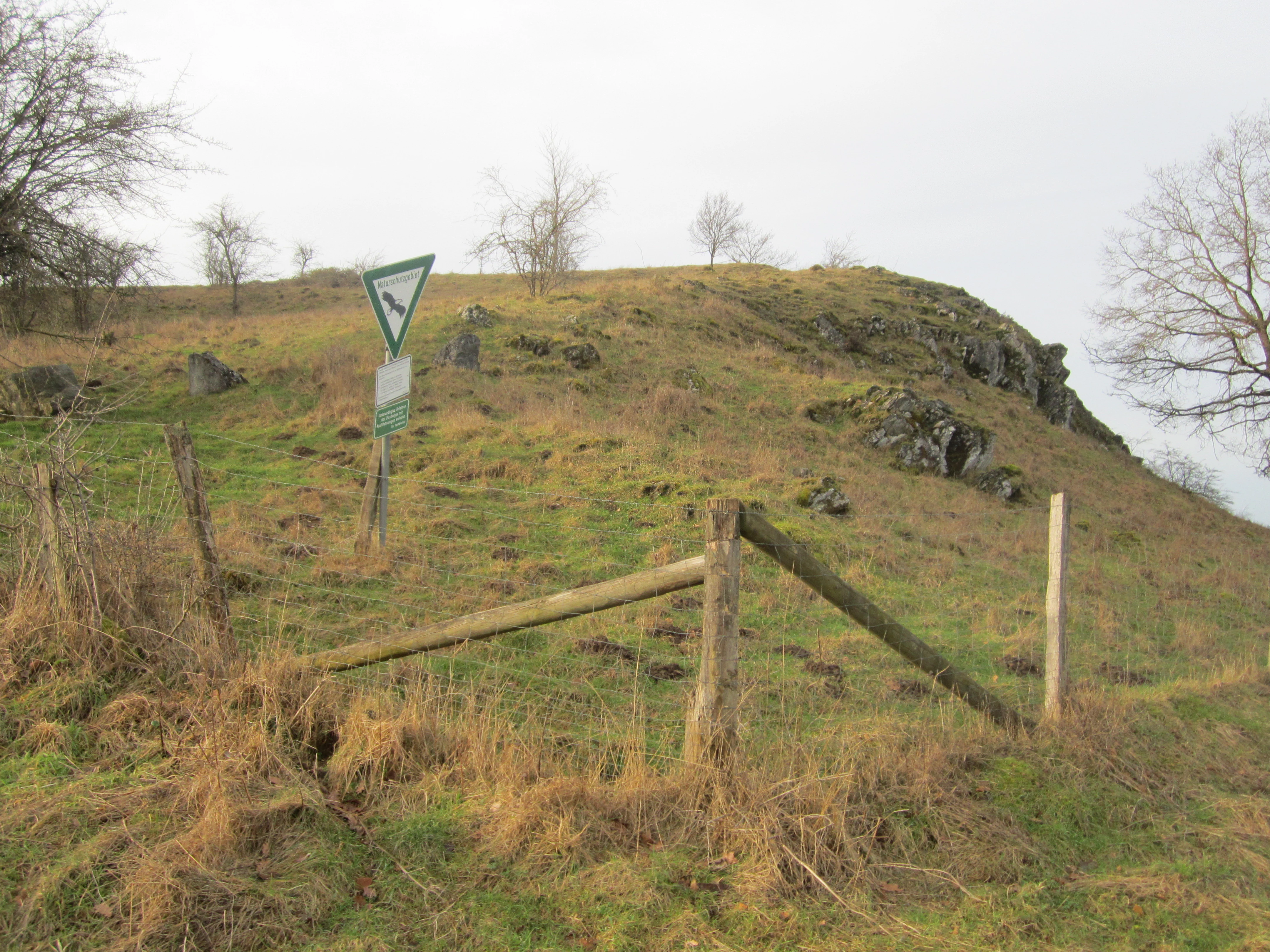 A triangular nature reserve sign stands on a grassy slope with limestone rock outcrops and a wooden fence.
