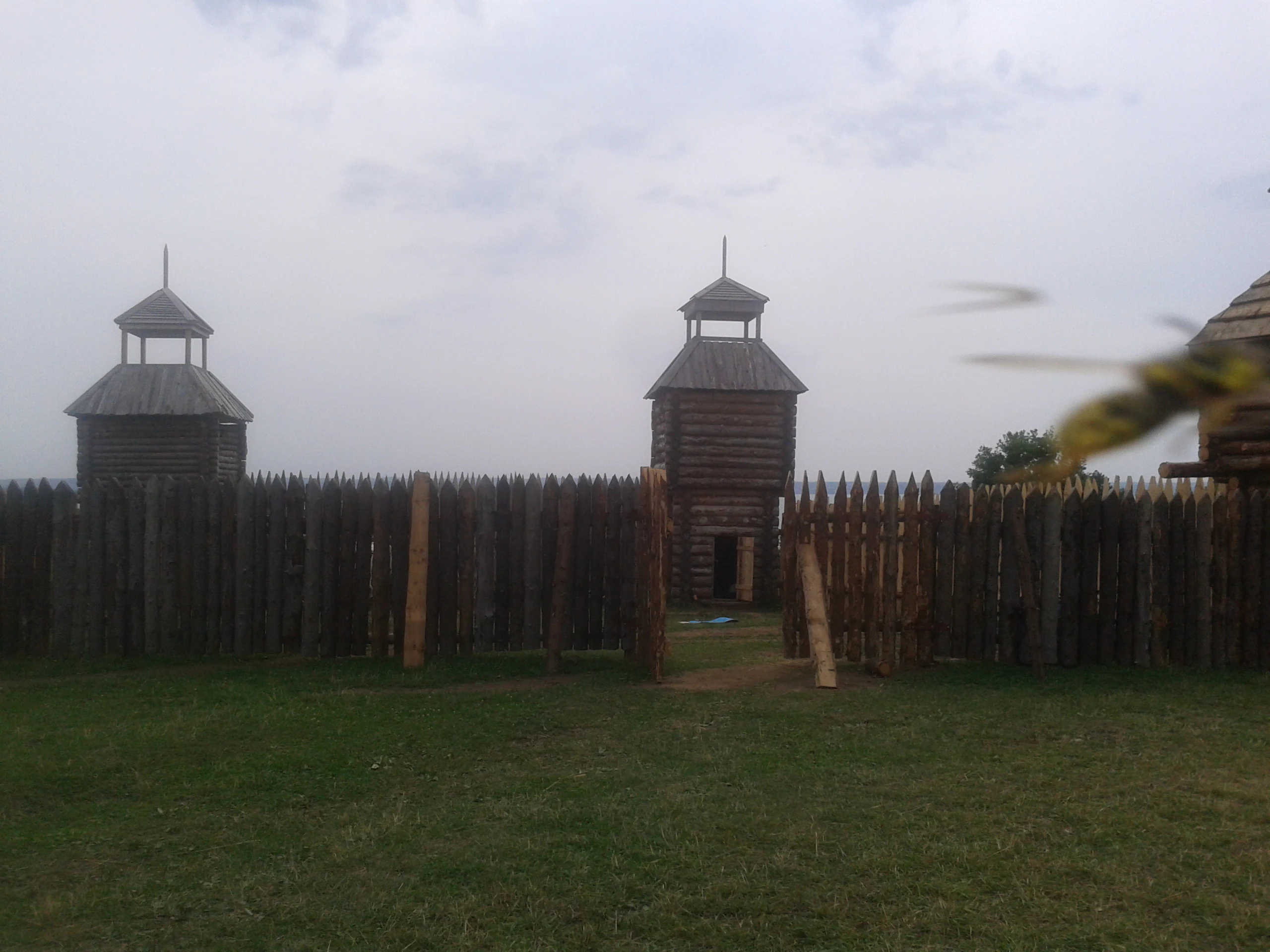 A line of wooden palisade fencing with two watchtowers under a cloudy sky.