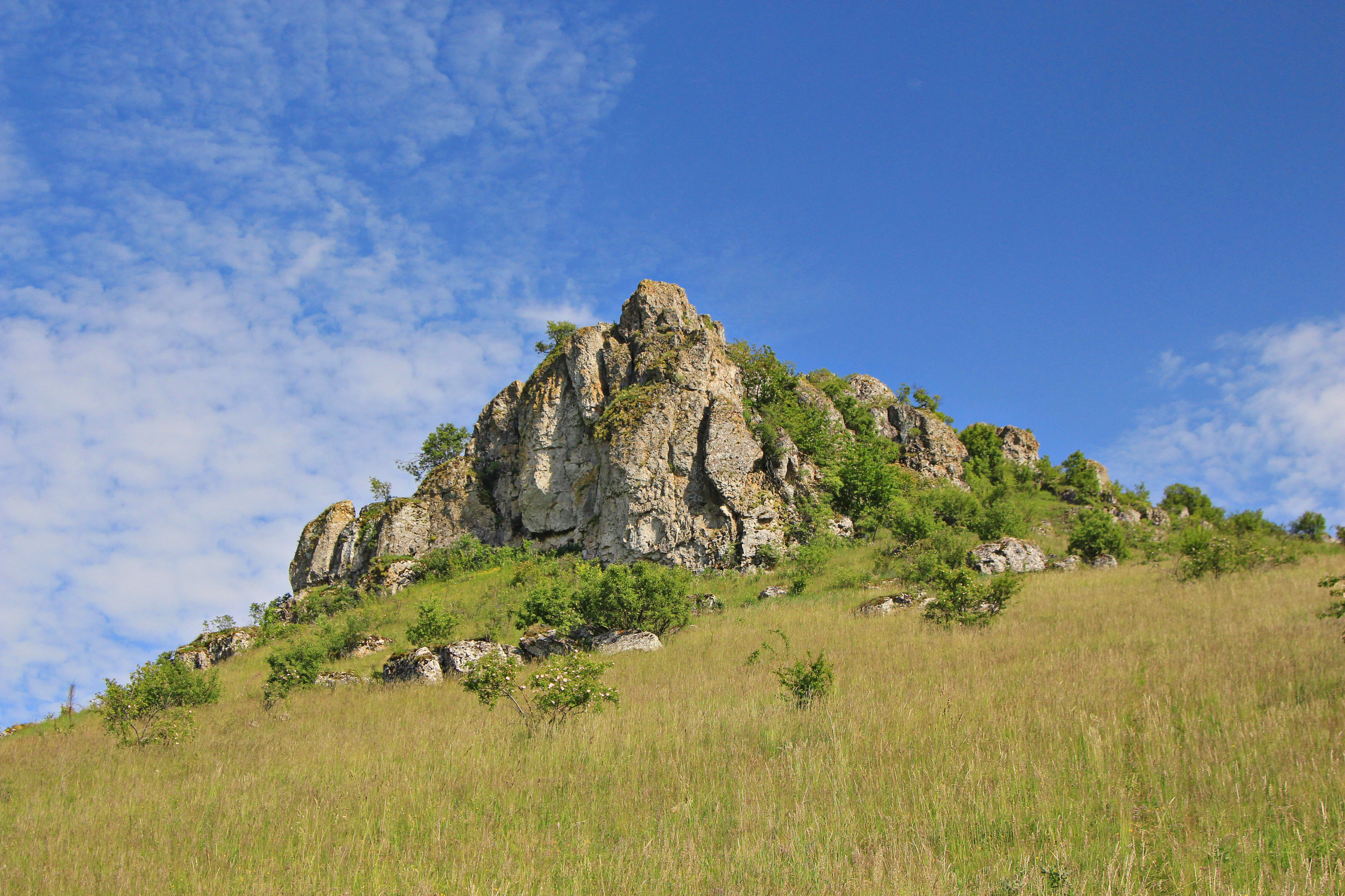 Grassy hillside with a rocky outcrop under a clear blue sky with scattered clouds