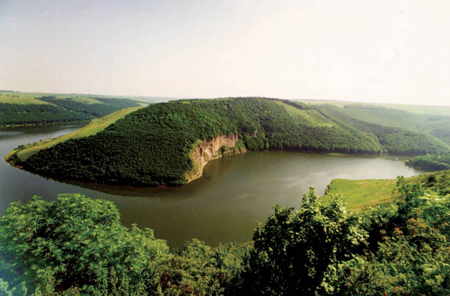 Wide-angle view of a river meander surrounded by green forested hills and open grassy areas under a clear sky