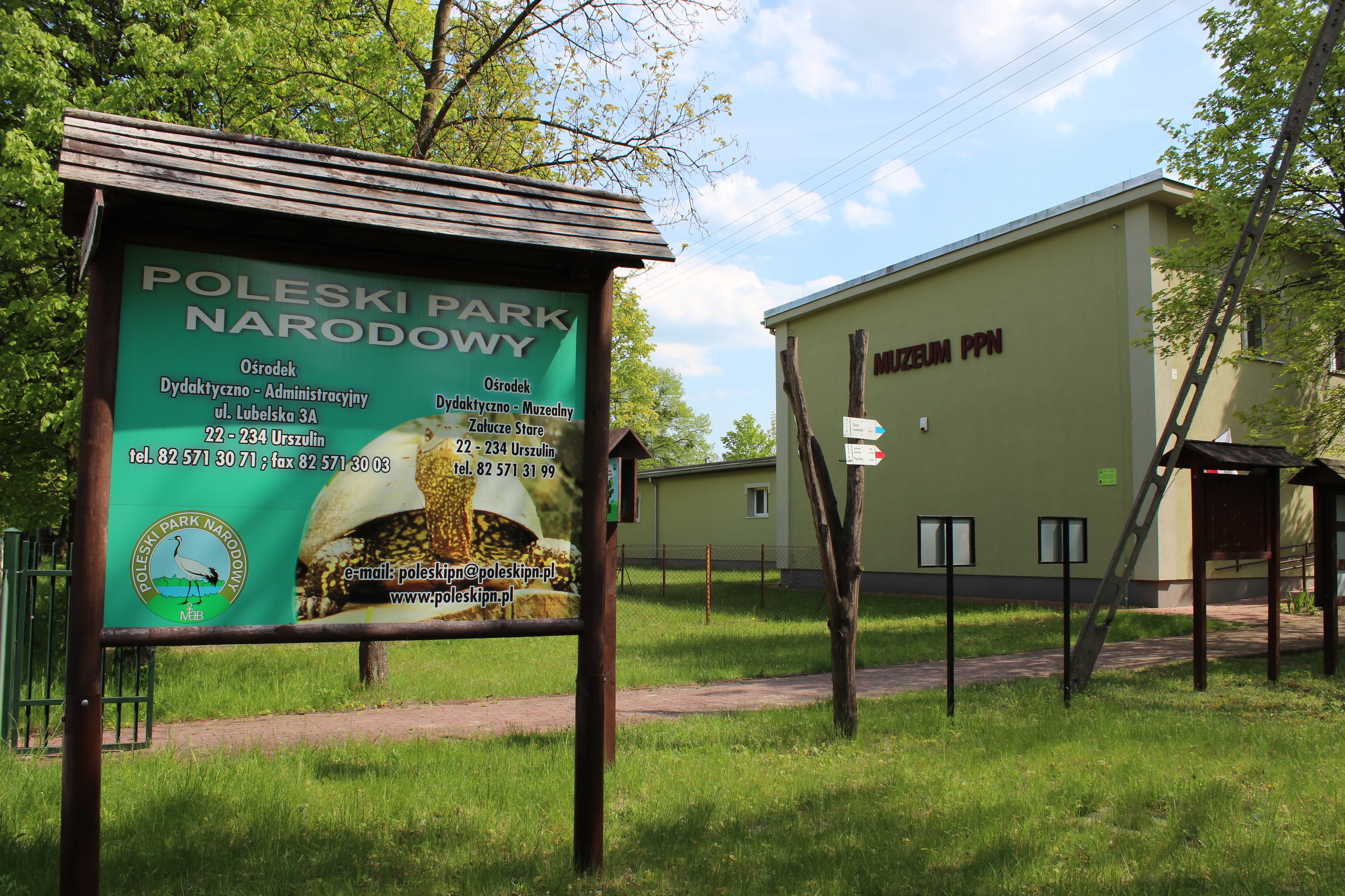 A green information board displaying the park name Poleski Park Narodowy, standing in front of the park museum building in Stare Zalucze.