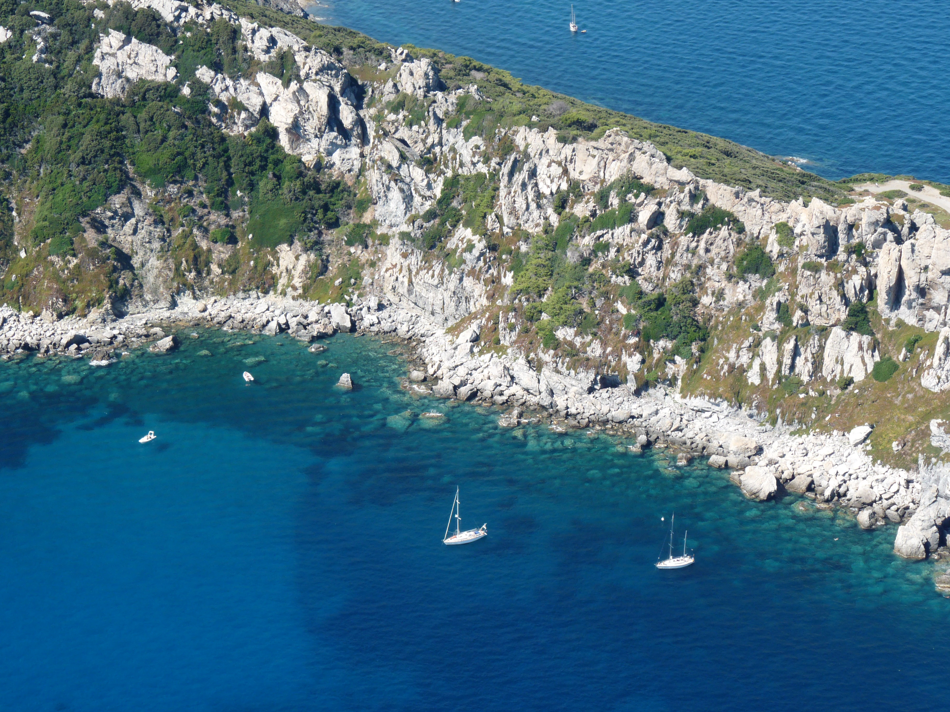 Aerial view of rocky coastline with clear blue water, sailboats, and green vegetation on Porquerolles Island.