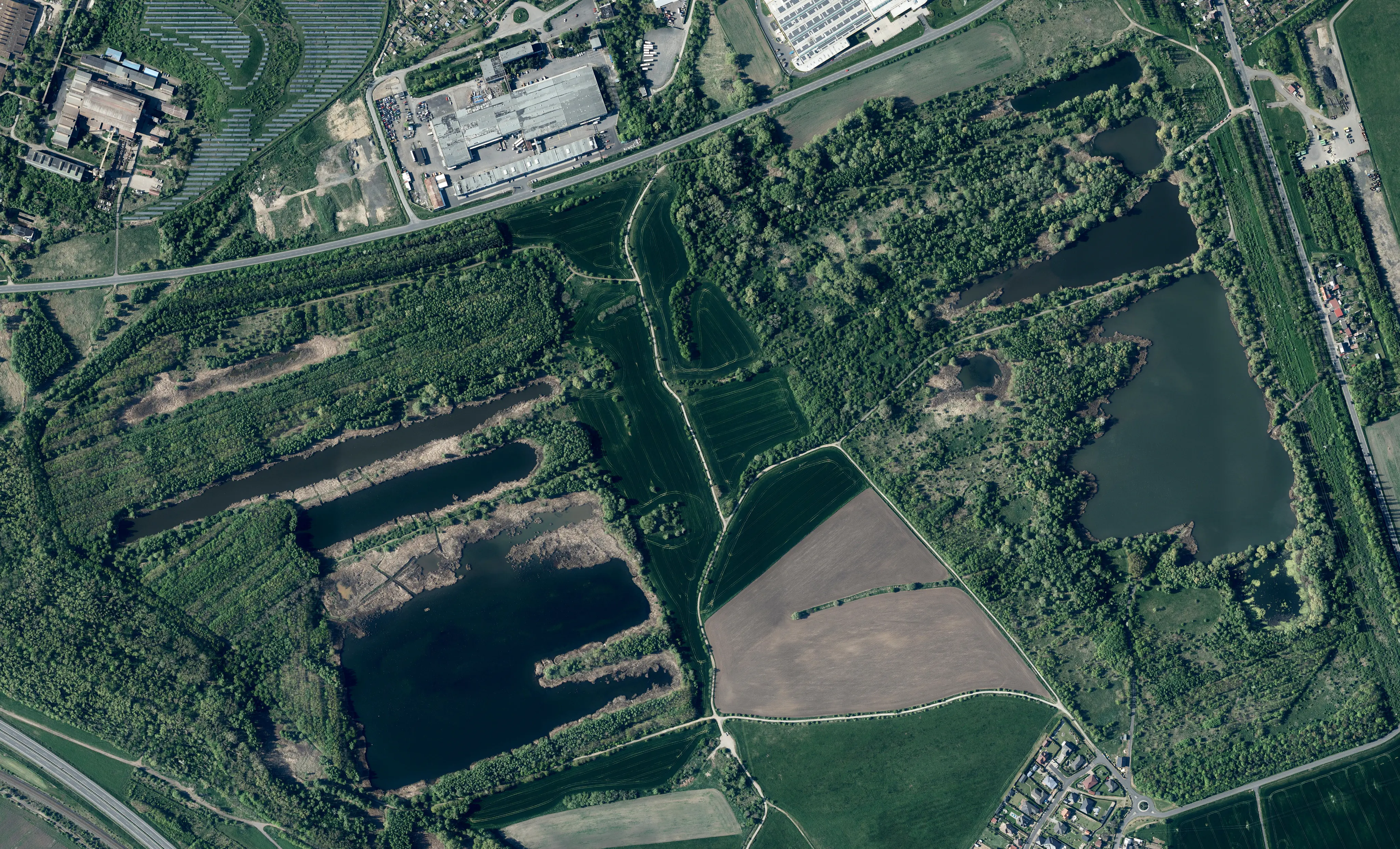 An aerial satellite photograph showing the Prazska pole nature reserve, featuring multiple ponds, forested areas, and adjacent industrial and agricultural land.