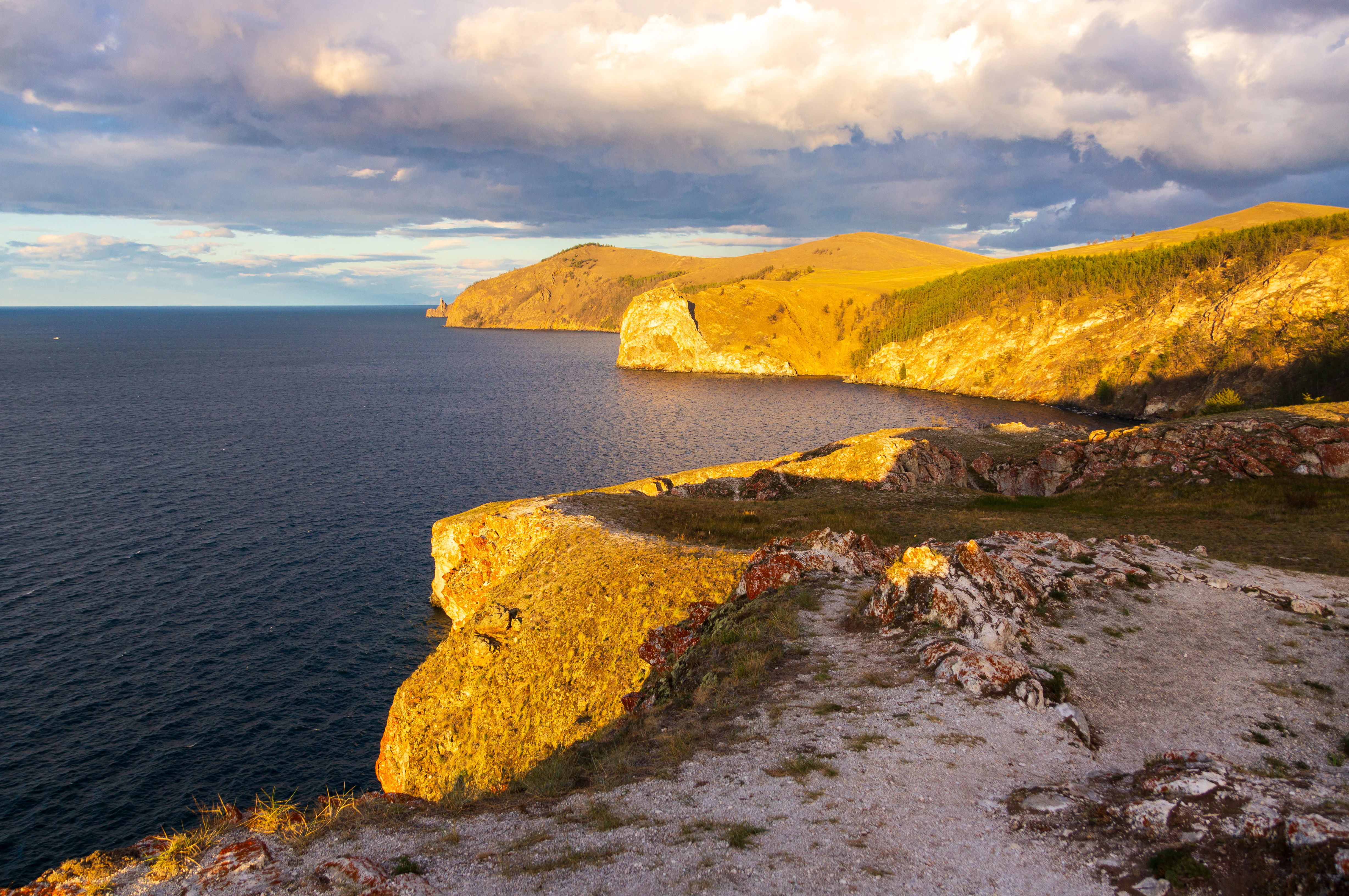 Rocky cliffside coastline view of Lake Baikal with golden light on cliffs and a partly cloudy sky