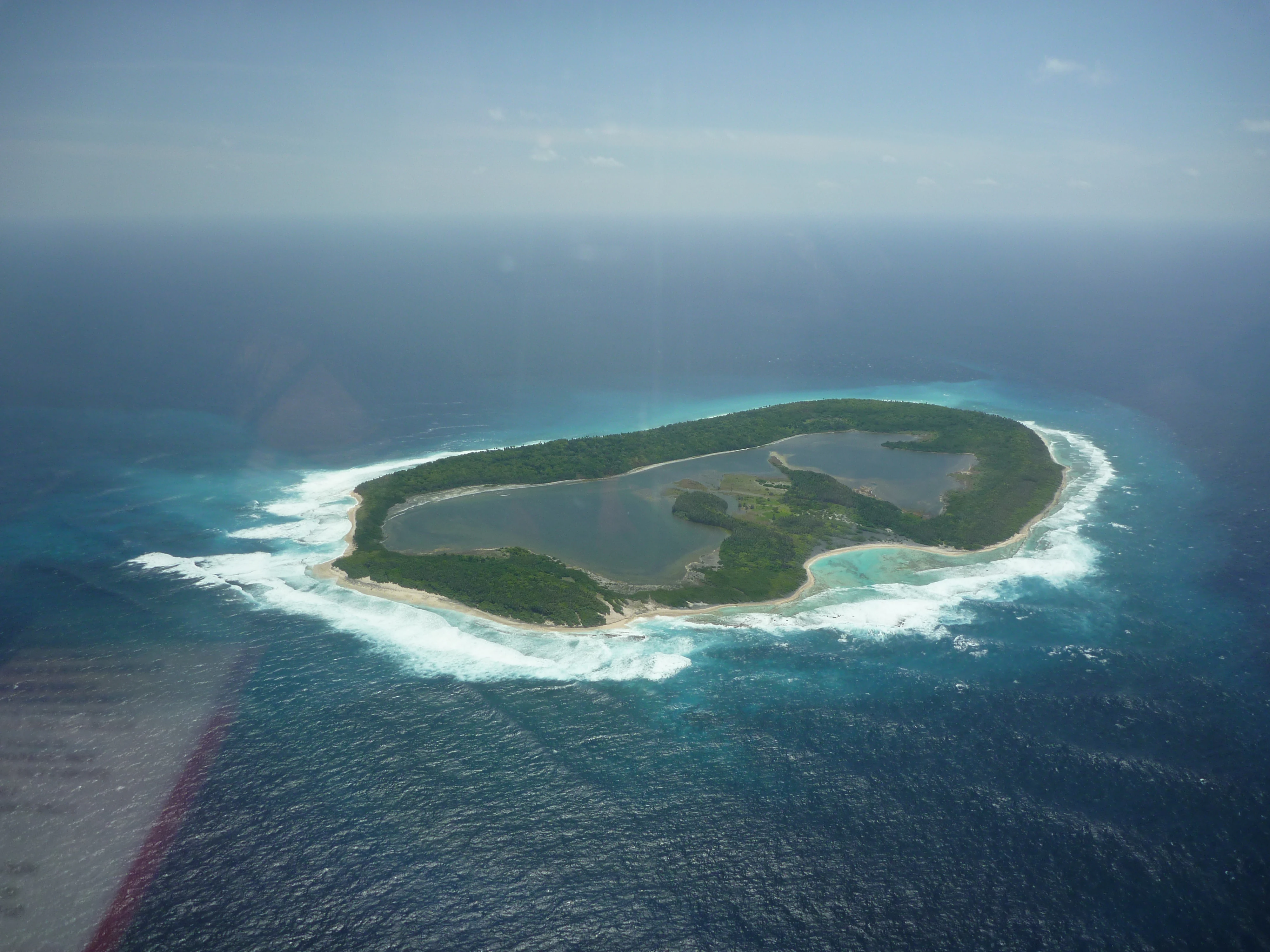 Aerial view of North Keeling Island showing a central lagoon, coastal vegetation, and turquoise ocean waters with white surf