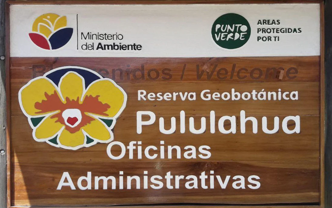 A wooden park entrance sign featuring the text Reserva Geobotánica Pululahua and Oficinas Administrativas, along with the Ecuadorian Ministry of Environment logo.