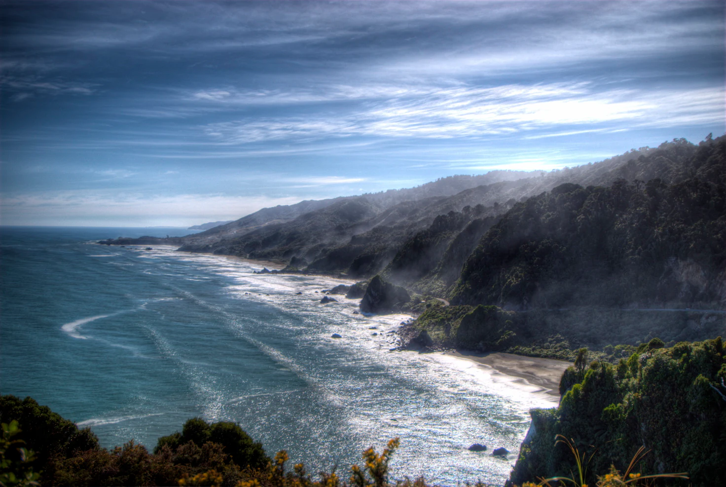 Vista panorámica amplia de una costa escarpada con acantilados boscosos y oscuros que se encuentran con una playa de arena y el mar de Tasmania bajo un cielo sombrío.