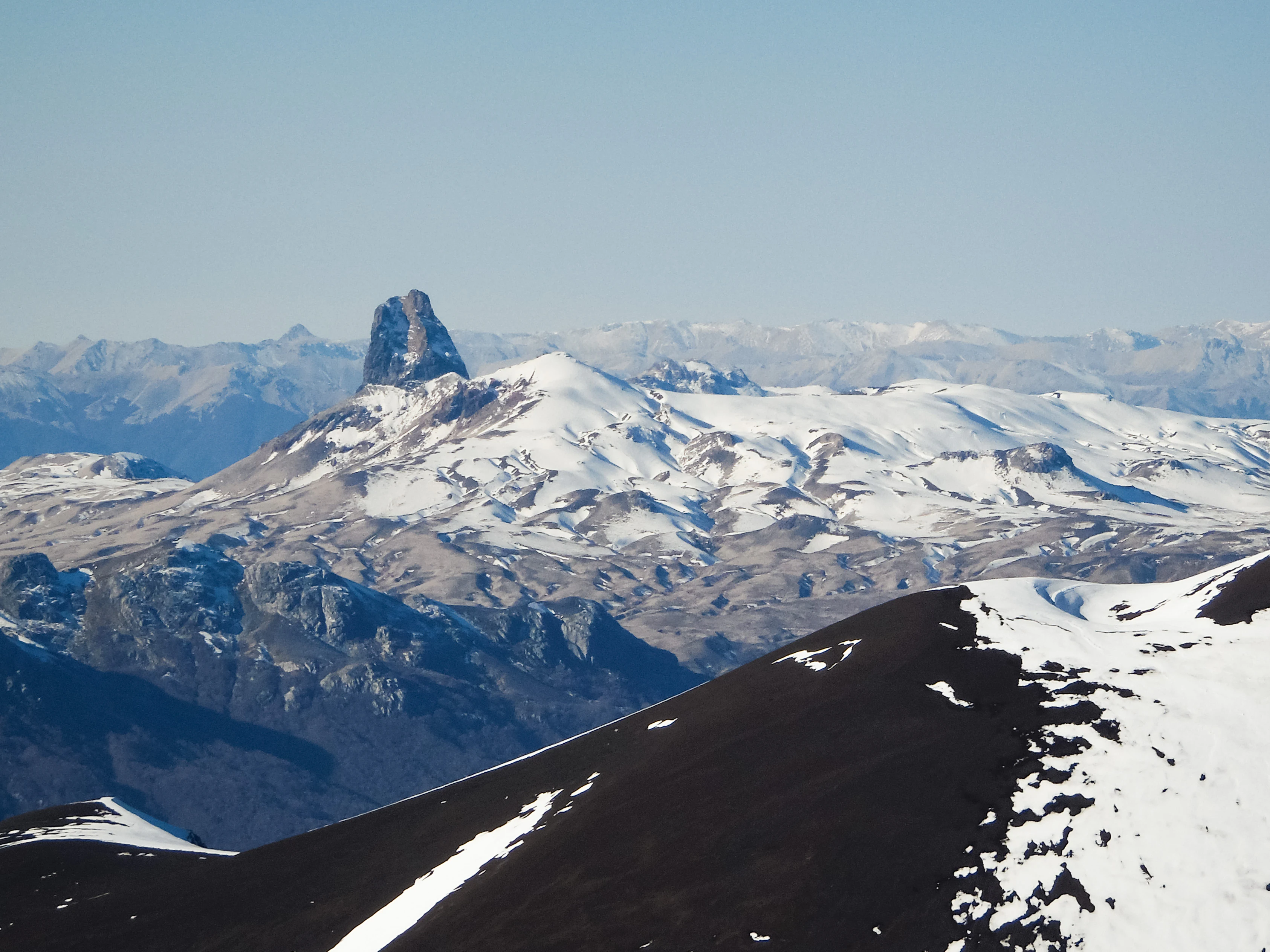 Snow-covered mountain peaks with a prominent central peak under a clear blue sky