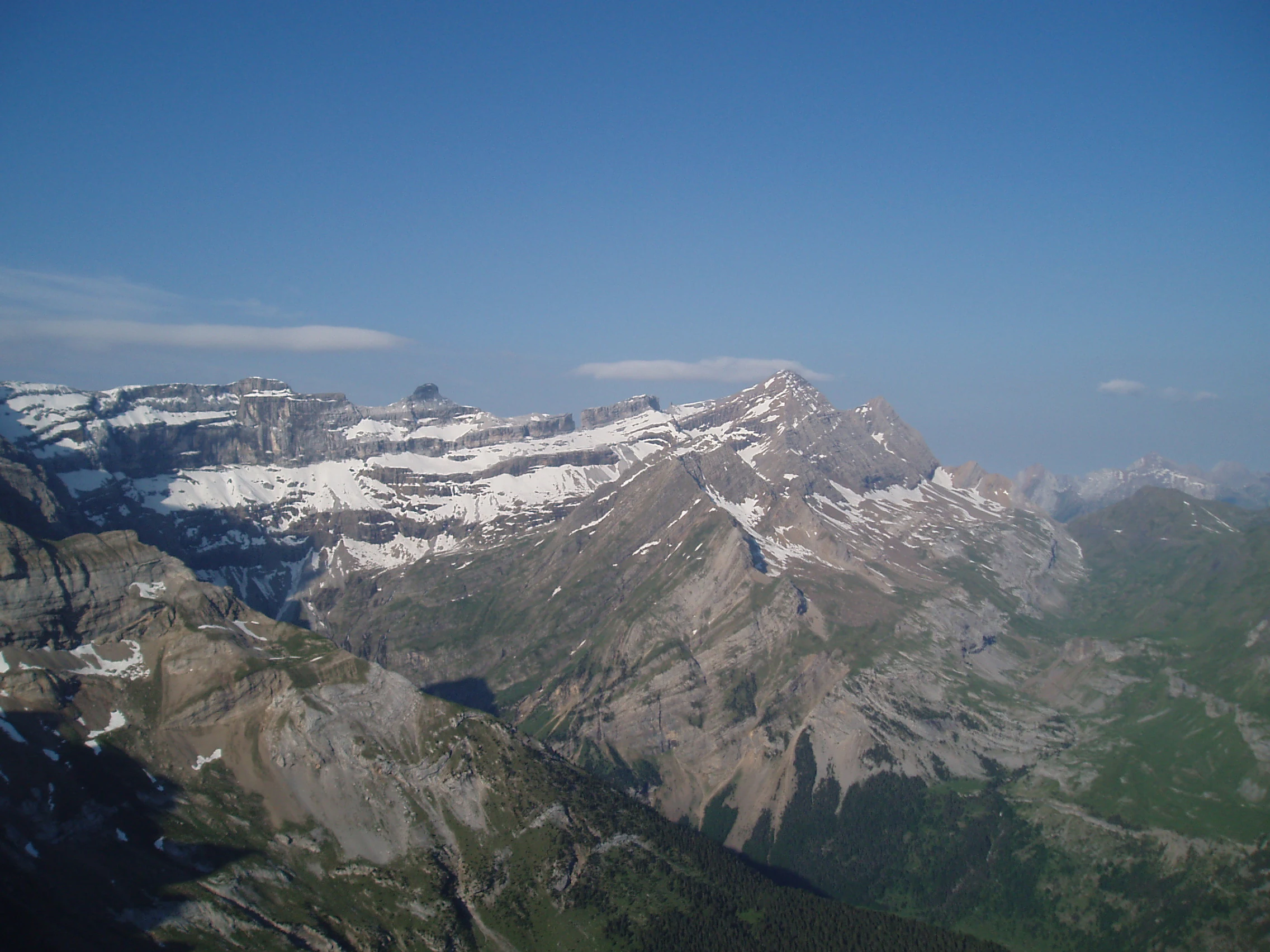 A vast, high-altitude mountain landscape featuring the rocky, snow-dusted ridges of the Cirque de Gavarnie under a clear blue sky.