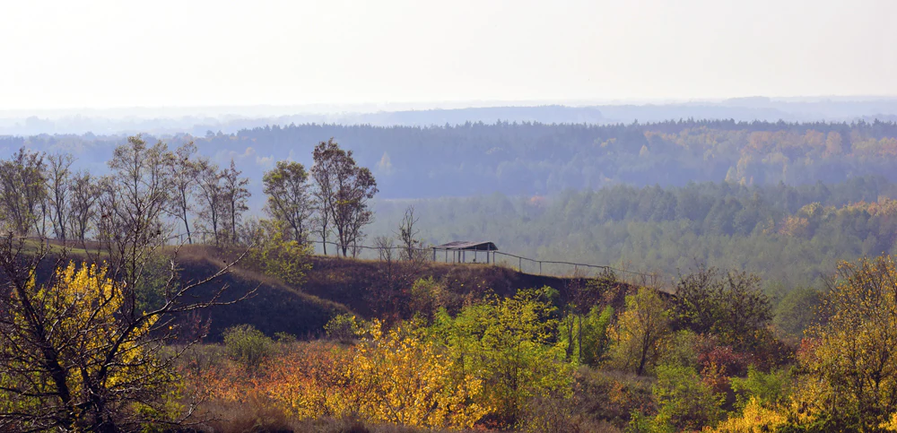 Rolling hills with autumn-colored trees, a small structure on the hilltop, and forested valley in the distance