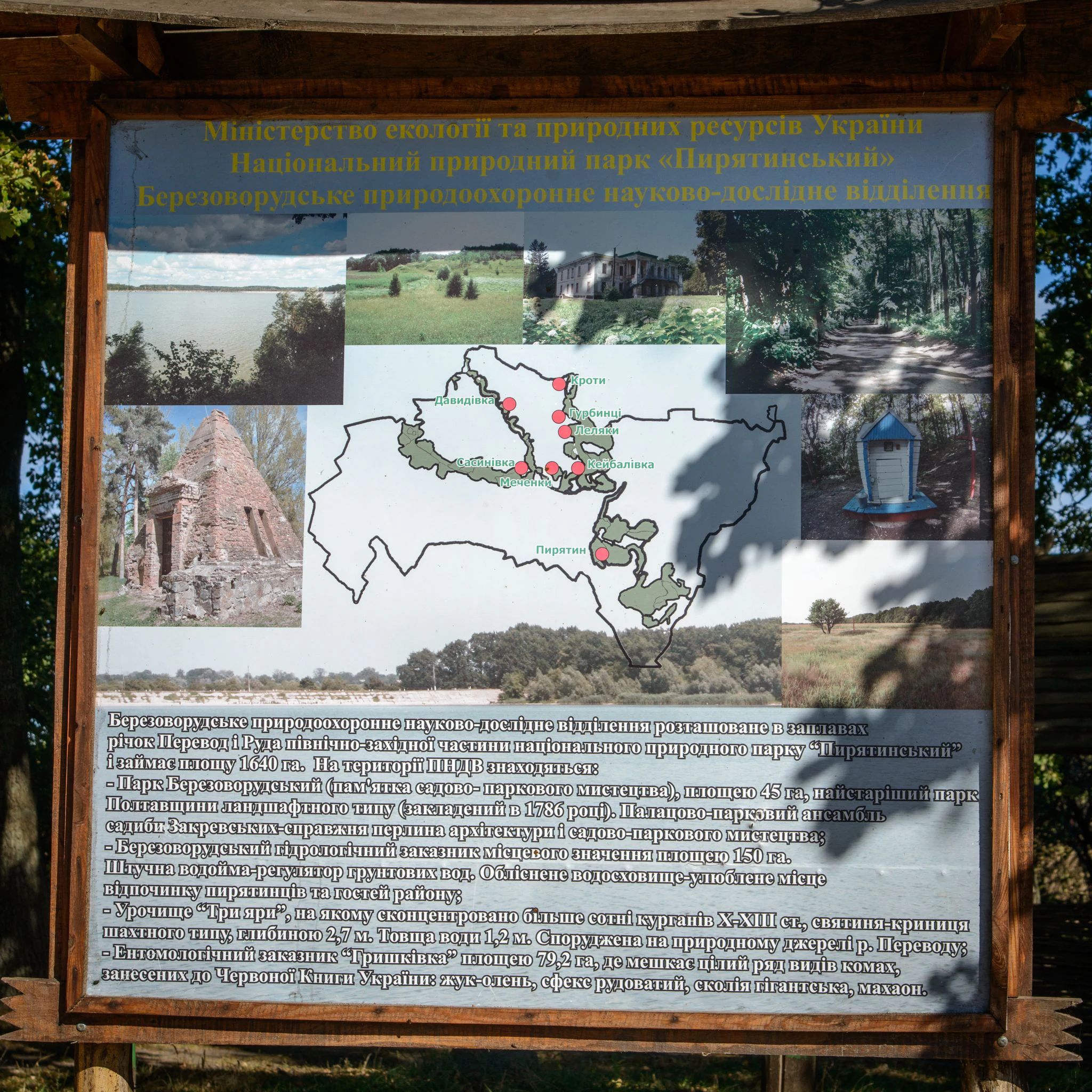 Wooden information board with Ukrainian text, multiple embedded images including landscape views, a map, and historical structures, displayed outdoors