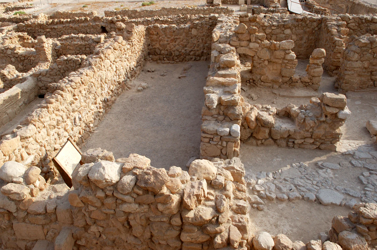 Stone ruins of ancient structures with walls and foundations in a desert setting, including a signboard
