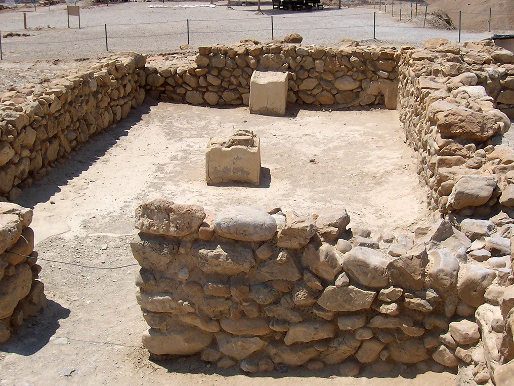 Stone-walled archaeological room with two stone structures in a sandy area within Qumran National Park