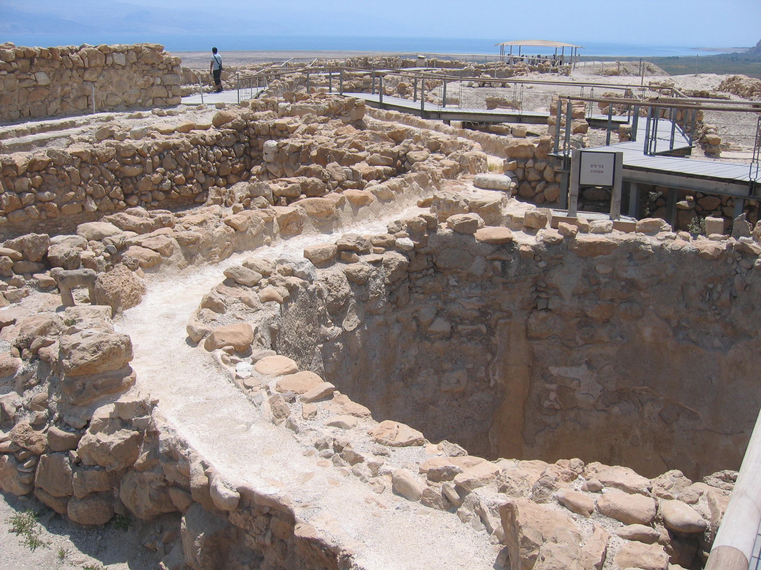 Stone cistern structure with surrounding ancient ruins and a person standing in the background