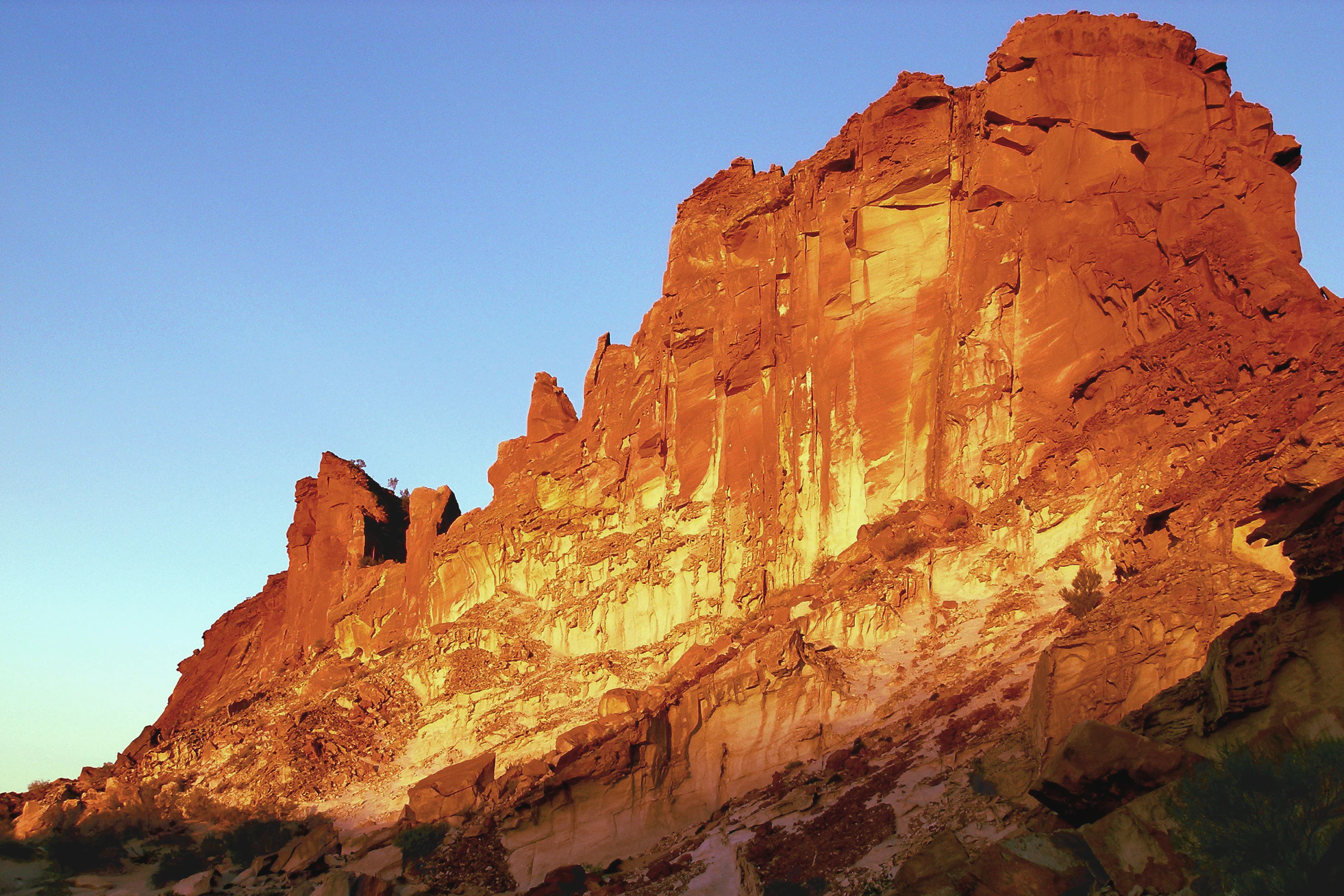 A large sandstone rock formation with deep red and orange colors lit by sunset against a clear blue sky in Rainbow Valley Conservation Reserve.
