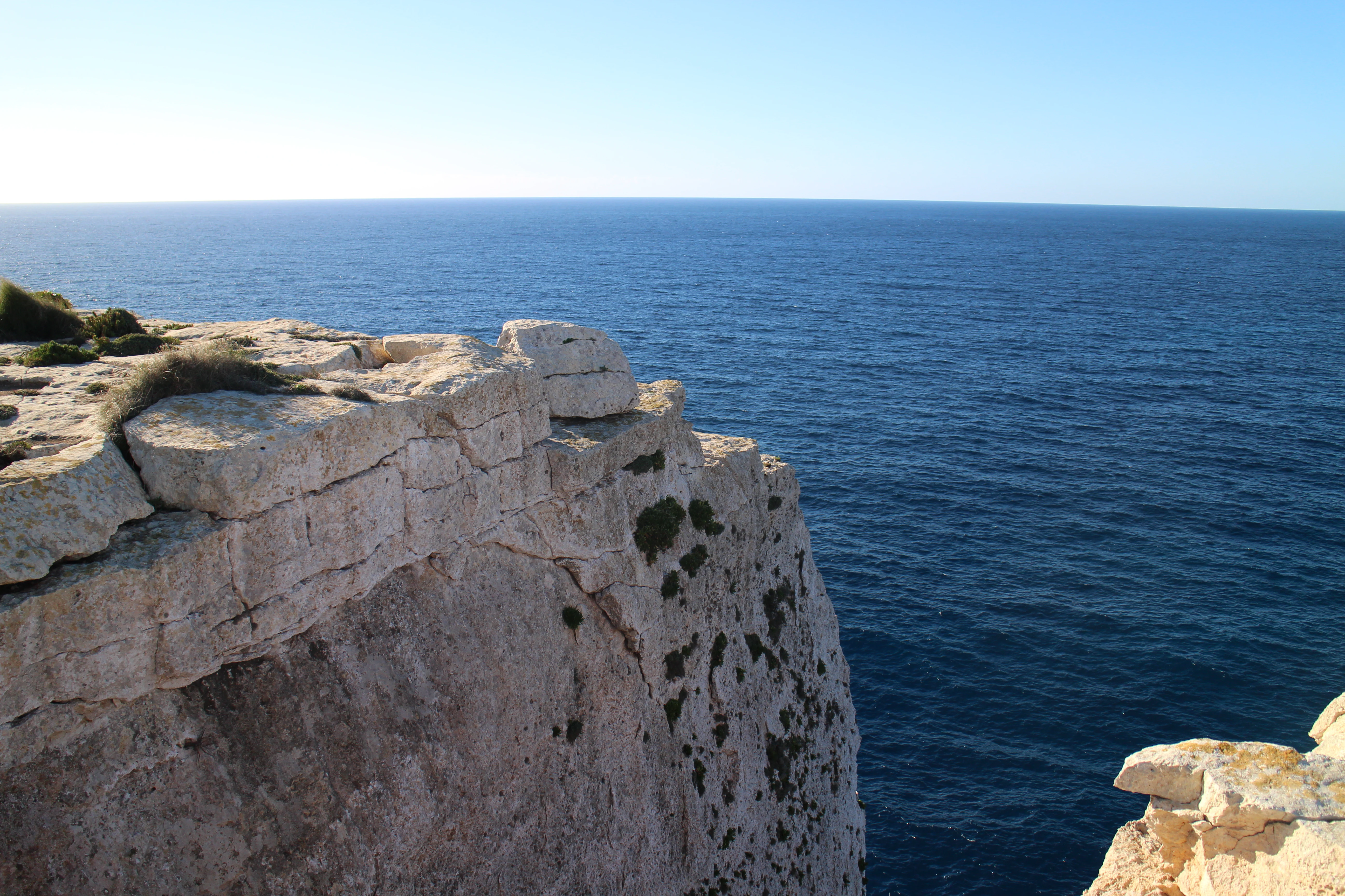 A steep limestone cliff face dropping into the deep blue Mediterranean Sea at Ras ir-Raħeb in Malta.