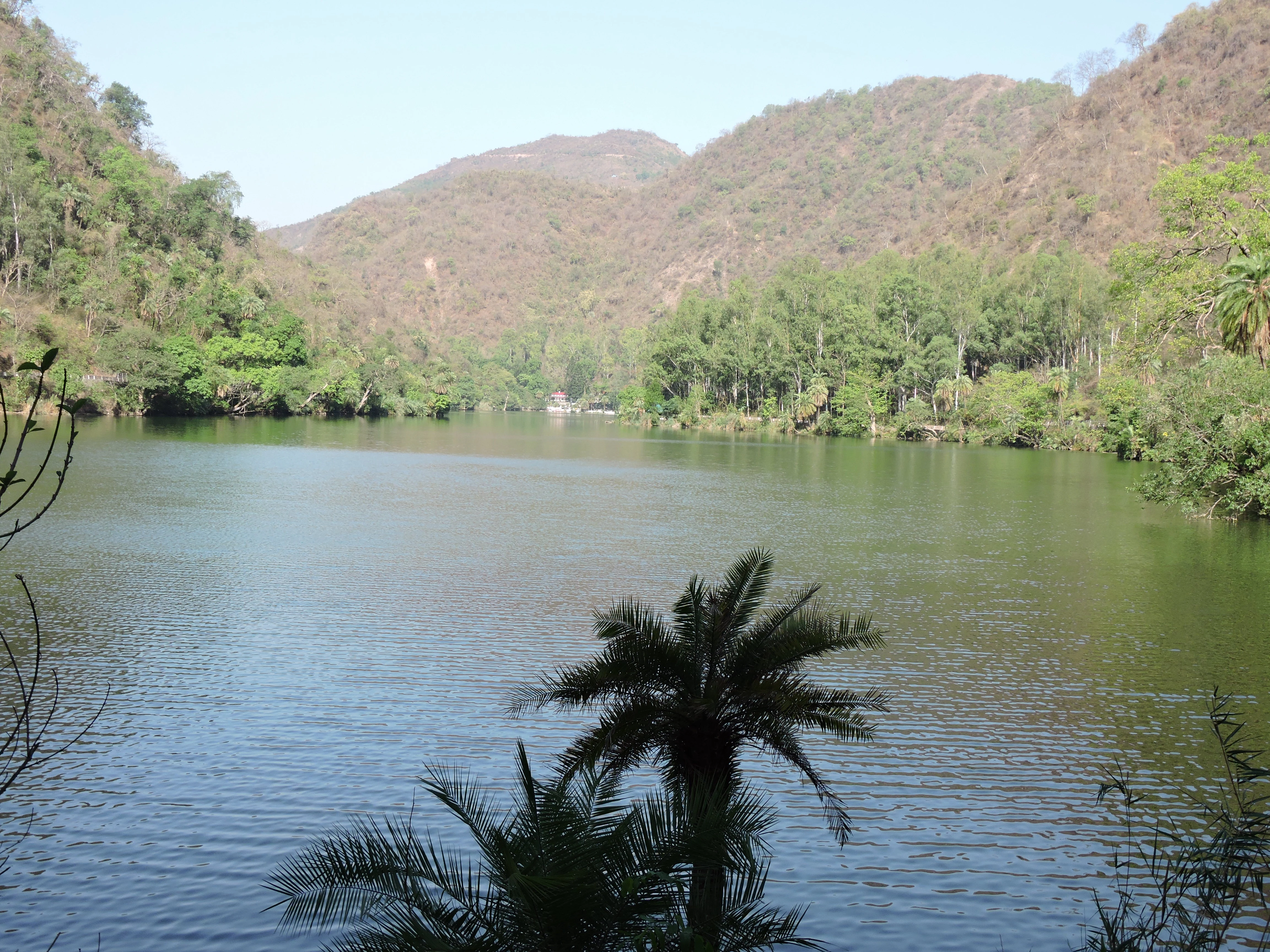 A wide shot of a calm lake surrounded by forested hills under a clear sky.
