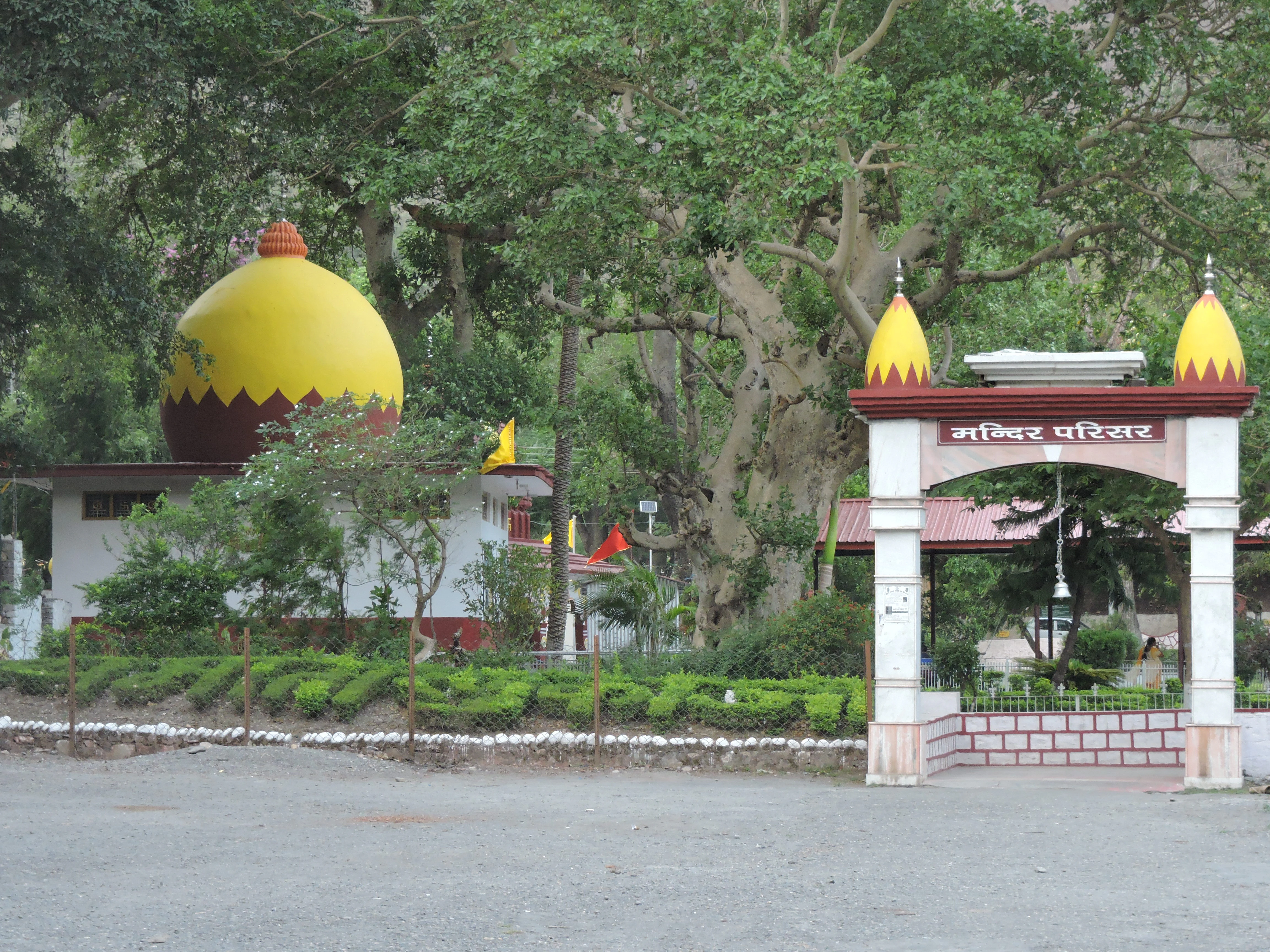 A white arched entrance gate with yellow domes leads into the Parshuram Temple complex, featuring a large yellow-domed building in the background surrounded by dense trees.