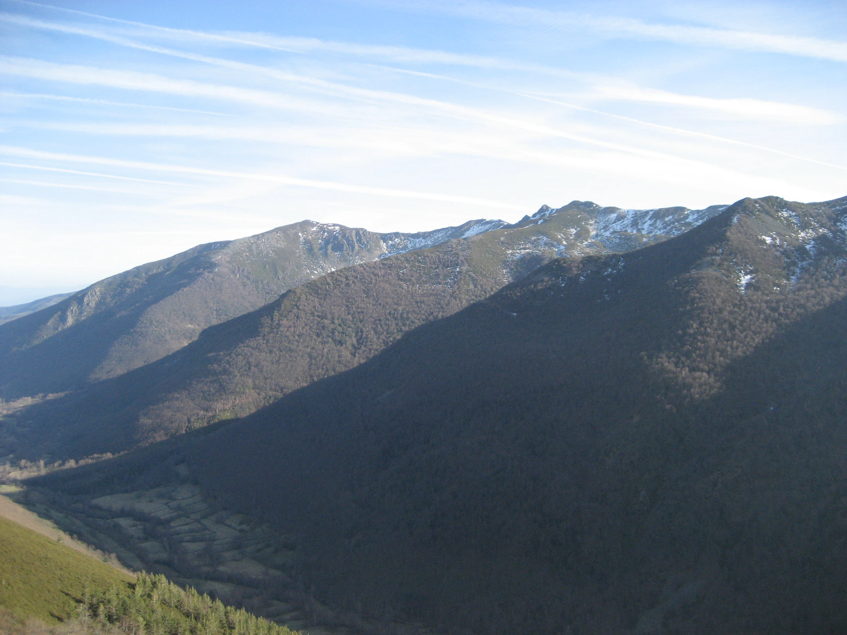 A wide view of rolling mountain slopes and ridges in the Ancares range, with patches of snow near the summits and a valley floor visible below.