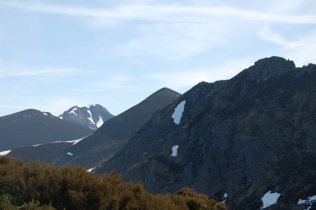 Un amplio paisaje montañoso bajo un cielo azul claro con restos de nieve en las laderas de picos rocosos y oscuros.
