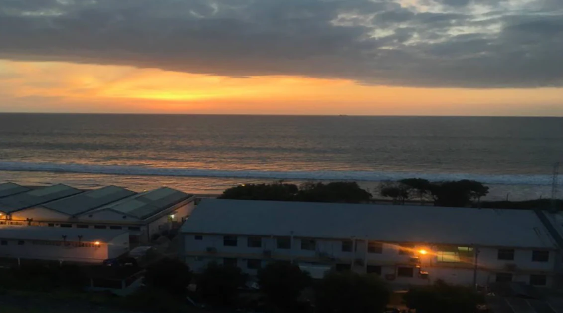 A wide angle sunset view over the ocean with buildings visible in the foreground along the coast.