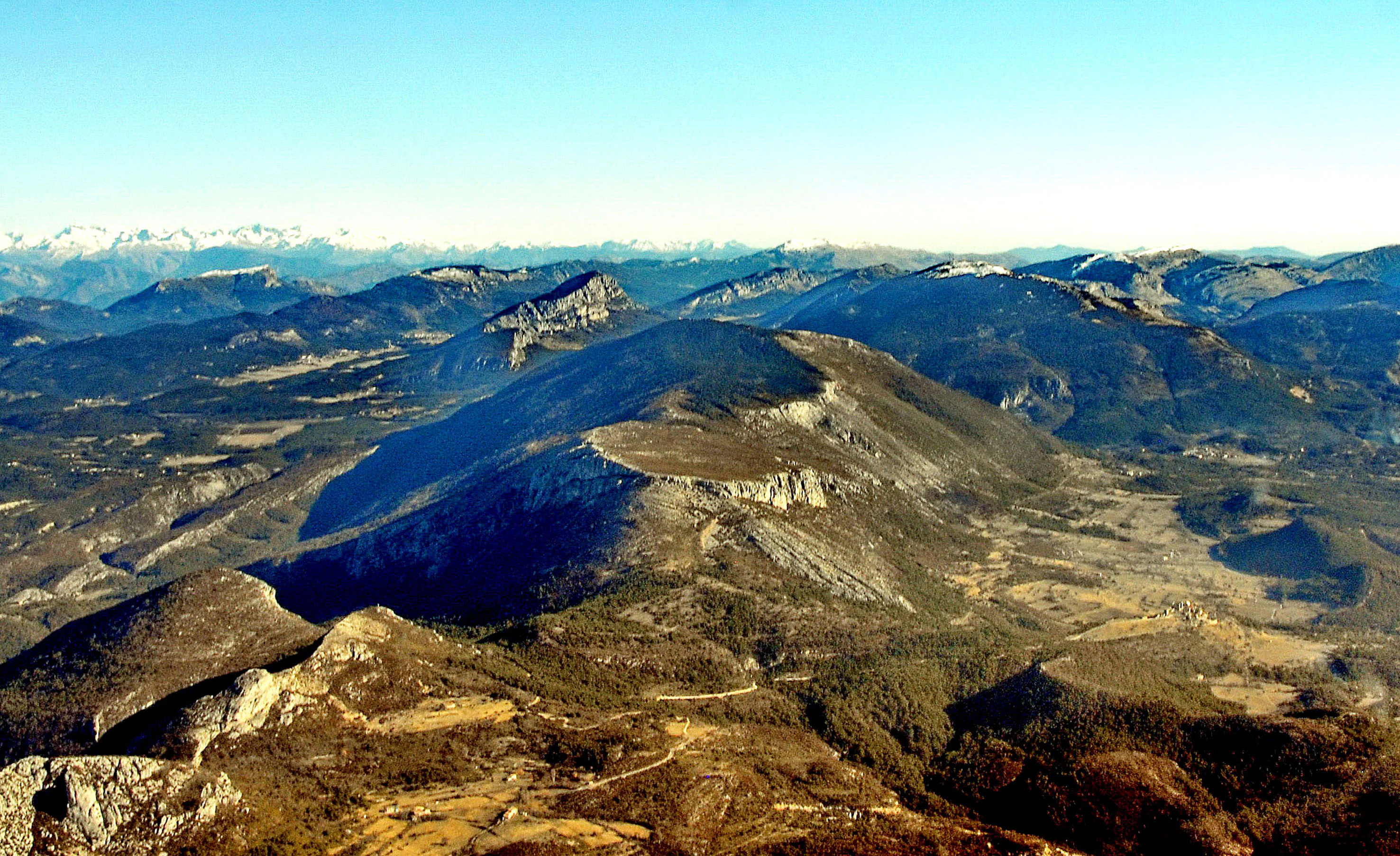 Wide aerial view of the rugged, mountainous landscape of the Haute-Provence region, featuring the Montagne de Brouis with distant snow-capped peaks in the background.
