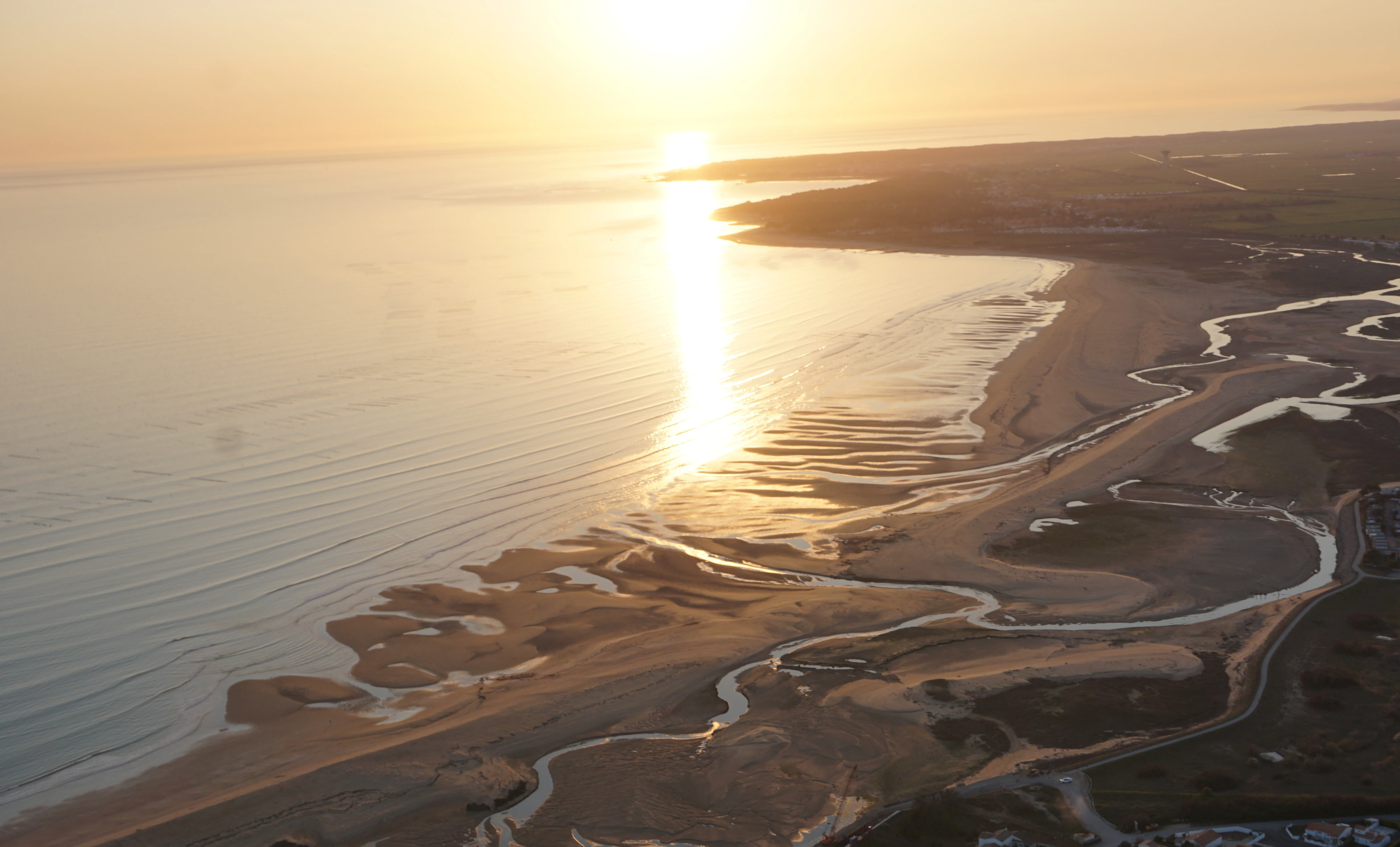 An aerial view of the Atlantic coastline at sunset, featuring winding tidal channels and sandy marshes in the Belle Henriette reserve.