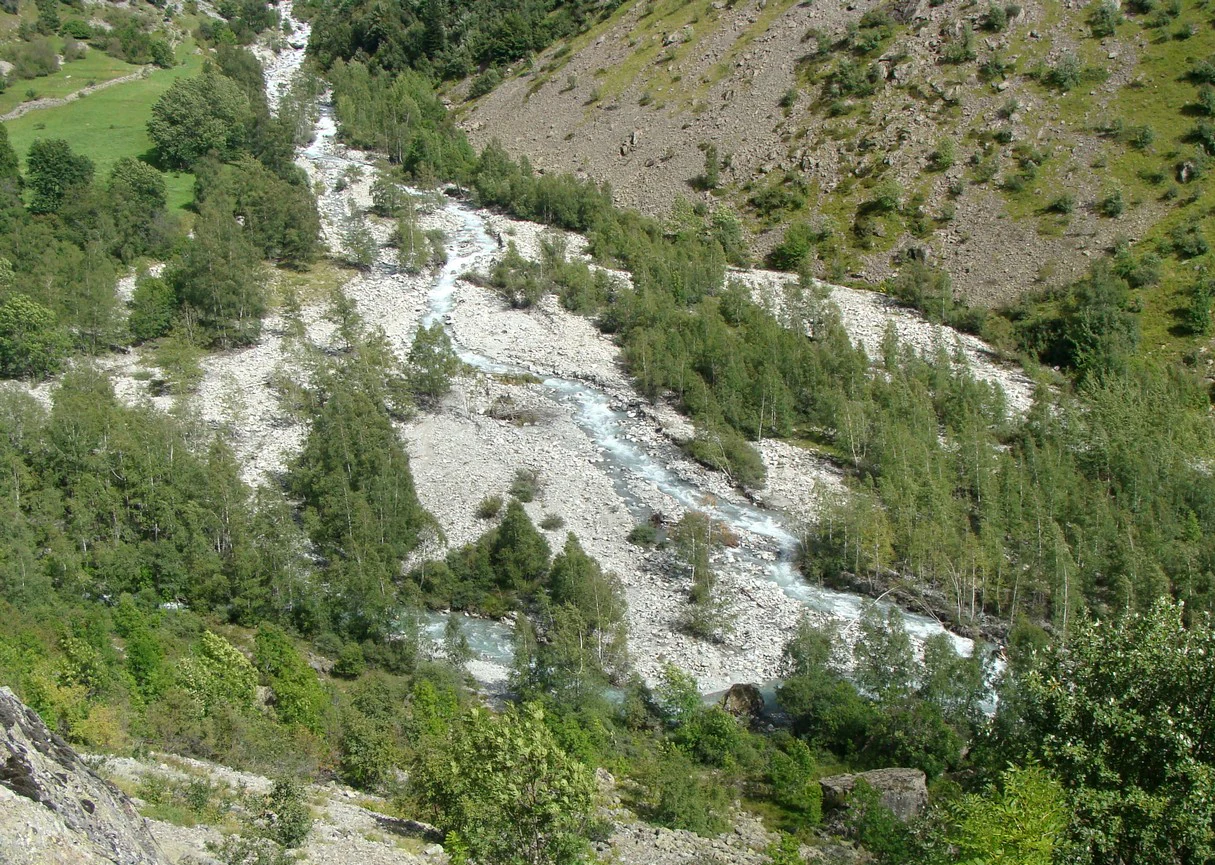 An aerial view of a mountain river flowing through a rocky, tree-lined valley in the Haute Vallée de la Séveraisse.