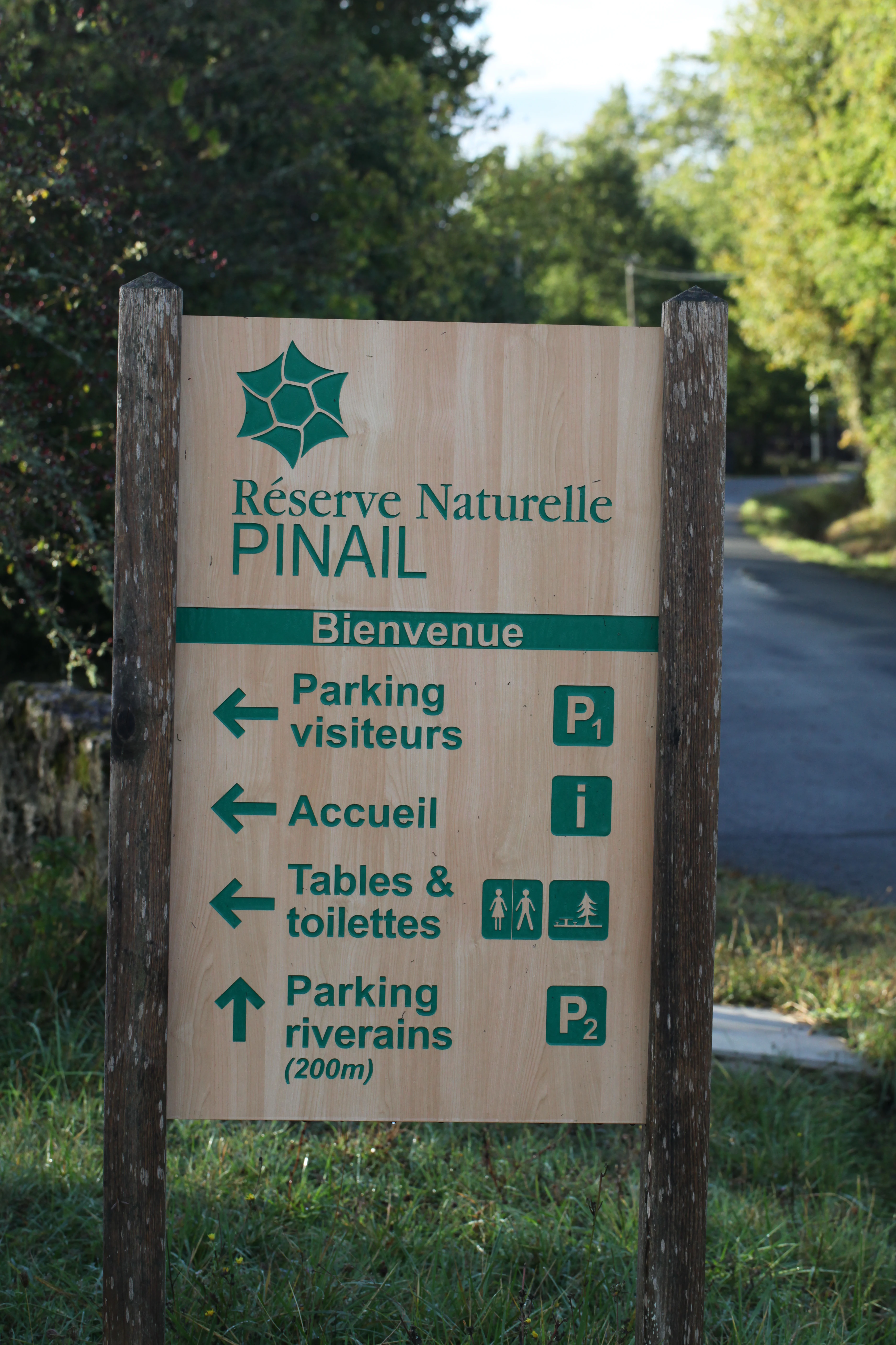 A wooden informational signpost for Réserve naturelle nationale du Pinail showing directions for visitors parking, reception, picnic tables, toilets, and residential parking.