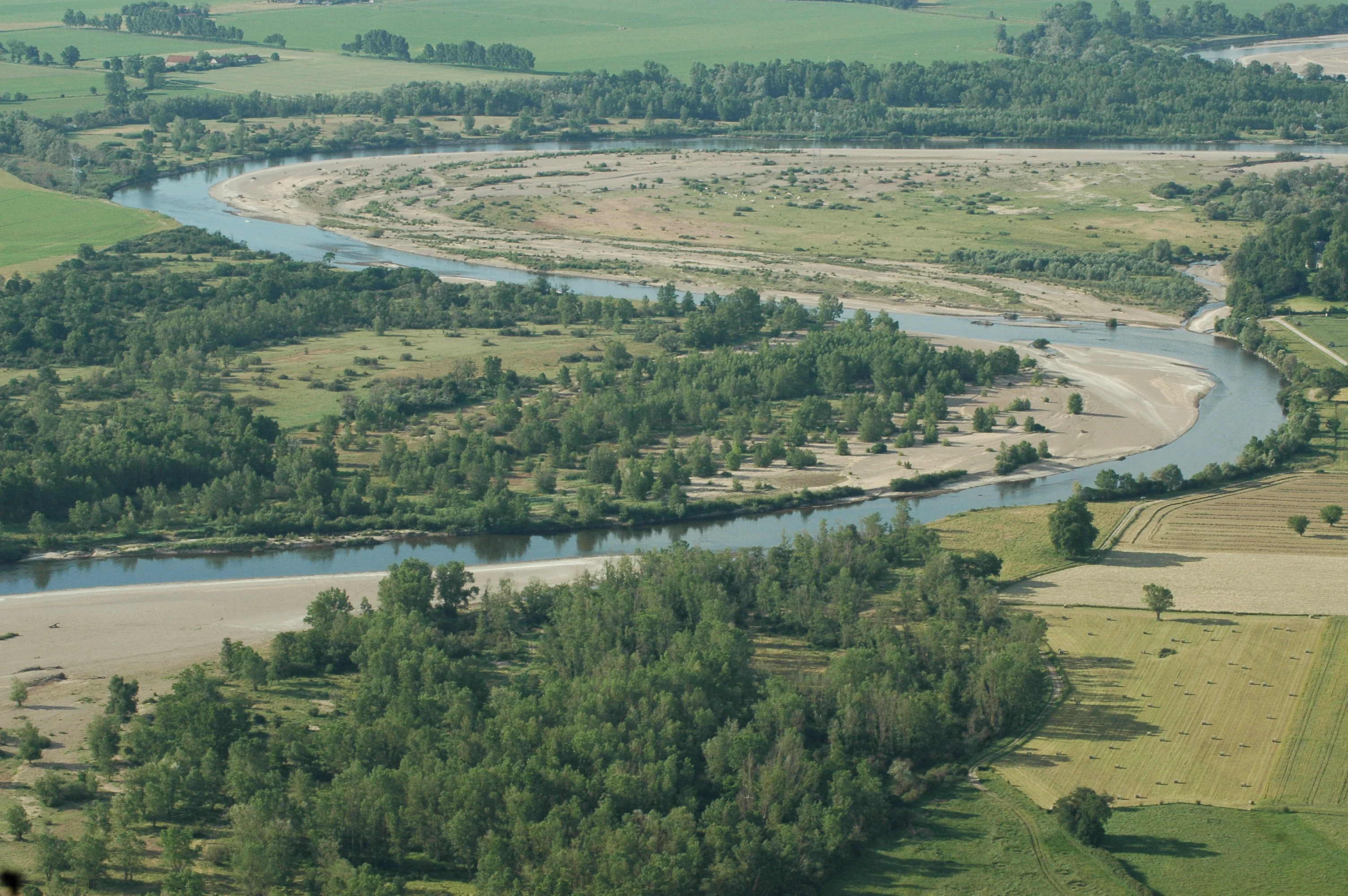 An aerial shot showing a meandering river with gravel bars surrounded by green riparian forests and agricultural fields.
