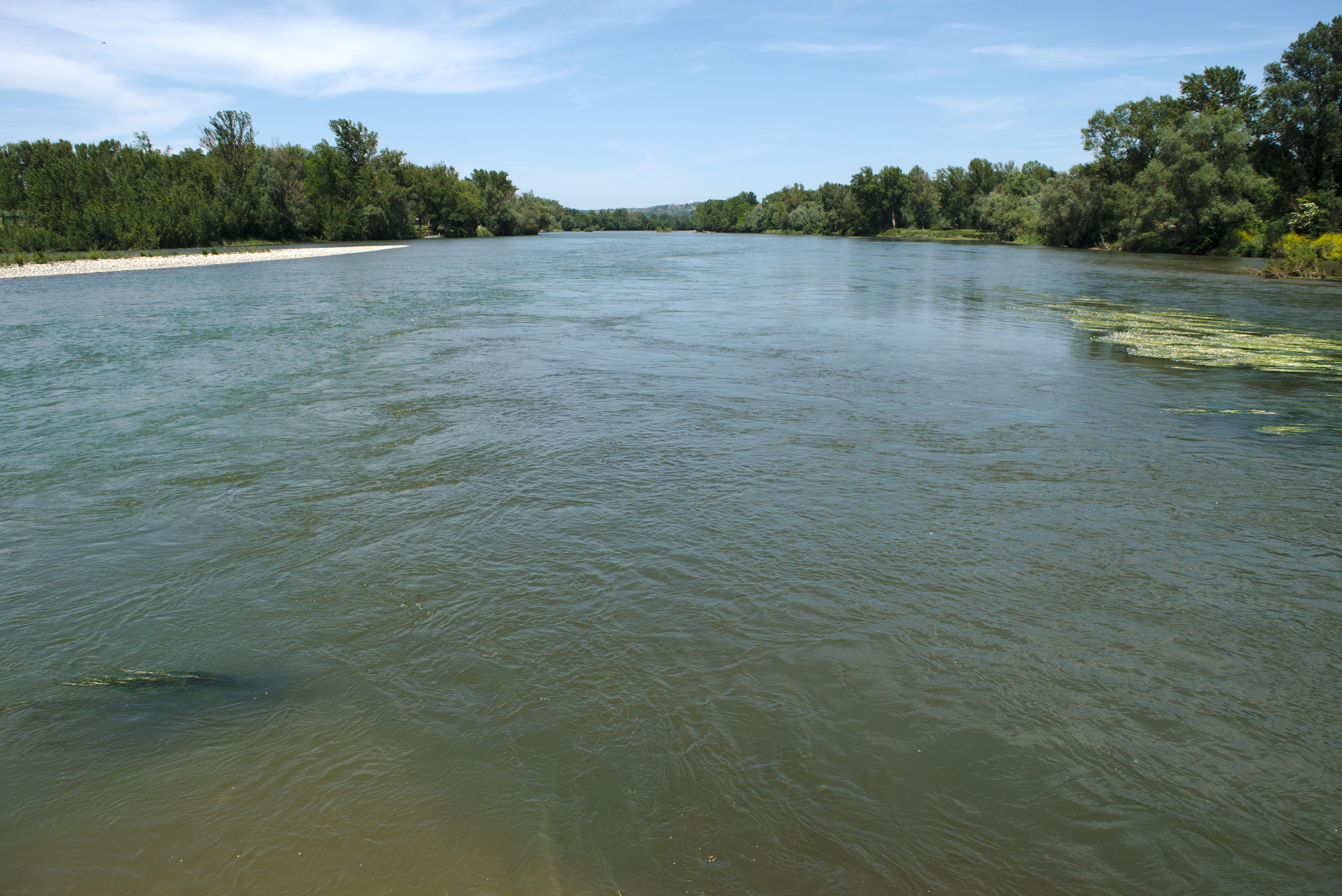 A wide view of the confluence of two rivers with forested banks and gravel shores under a bright sky.