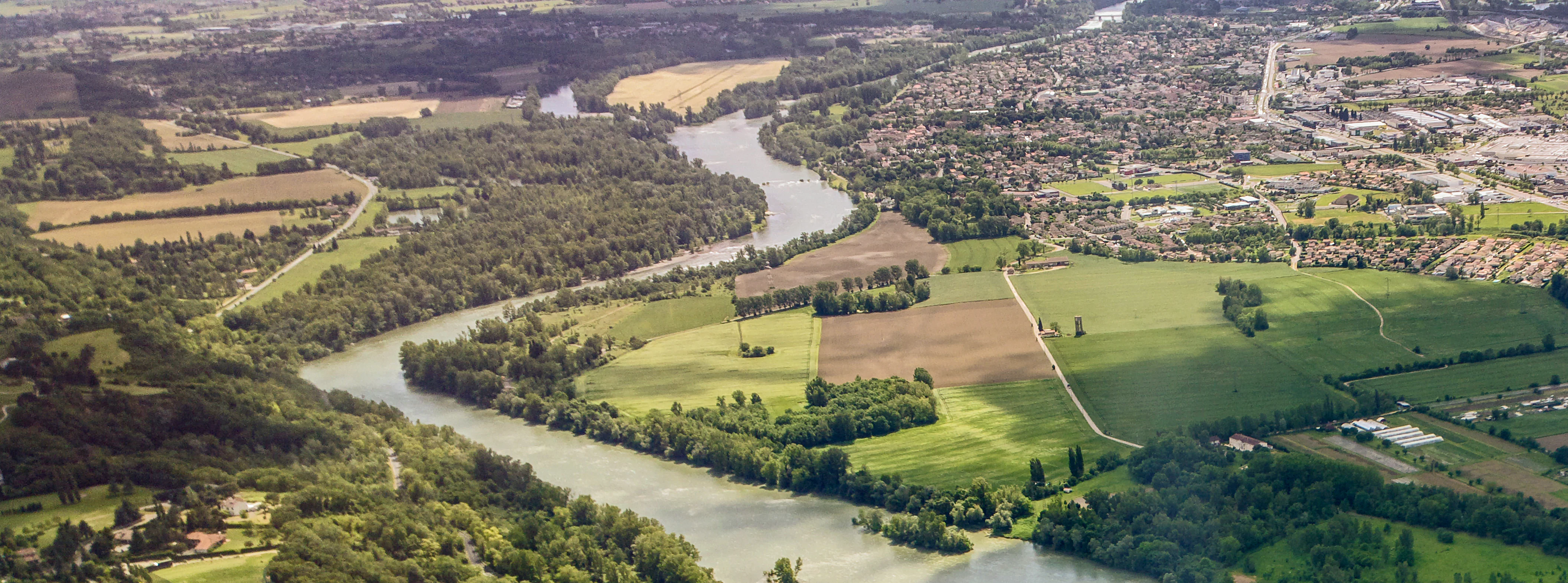 An aerial photograph looking down on the confluence of two winding rivers, with forested banks, agricultural fields, and a small town visible in the distance.