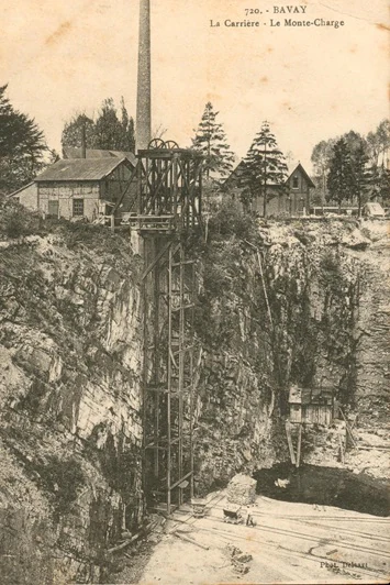 A vintage black and white postcard shows a sandstone quarry with industrial equipment, including a tall smokestack and a mechanical hoist structure, set against rocky cliffs and surrounded by trees.