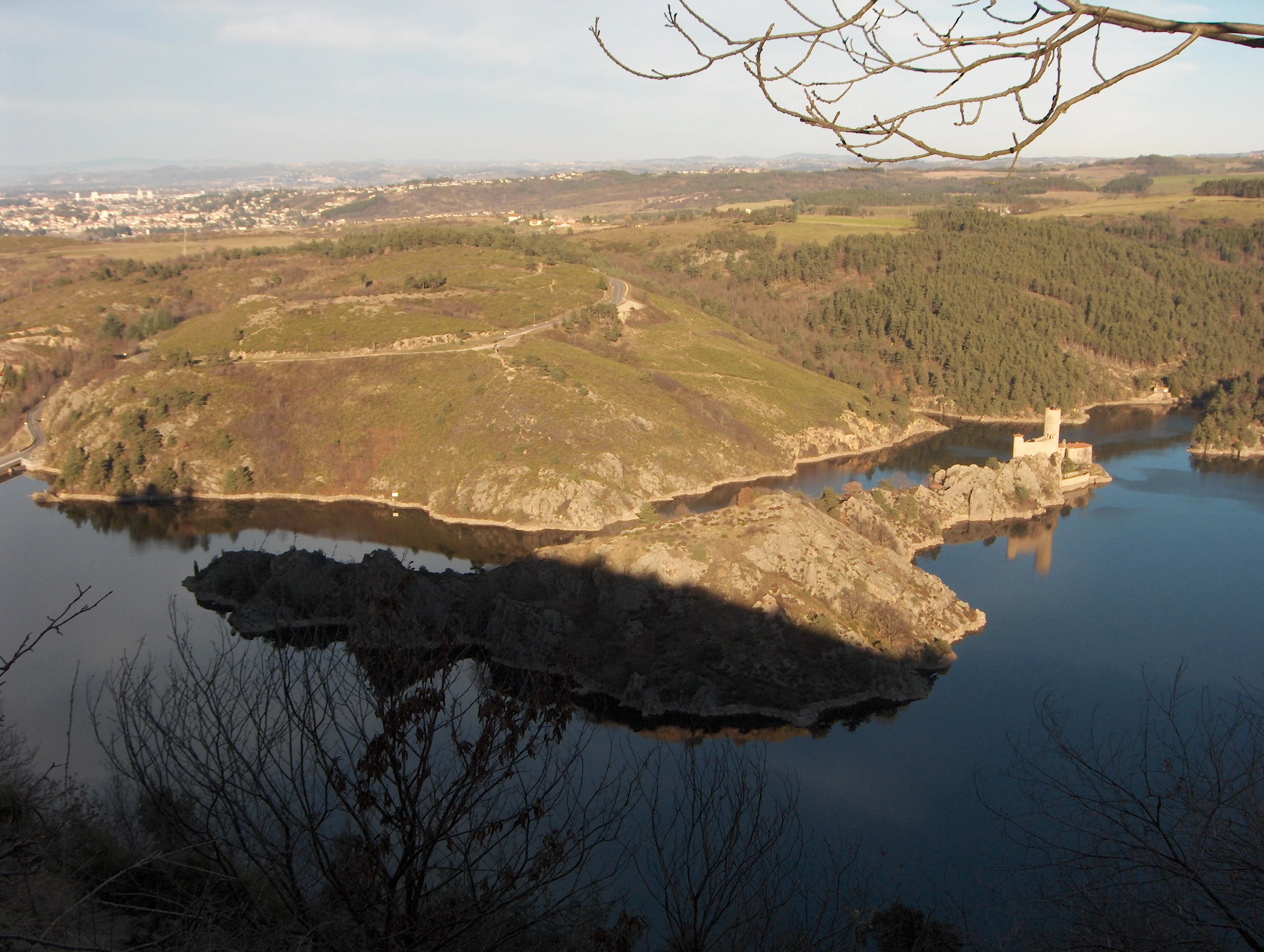 An aerial view of an island in a river featuring an old stone castle, surrounded by hills, forests, and calm water.